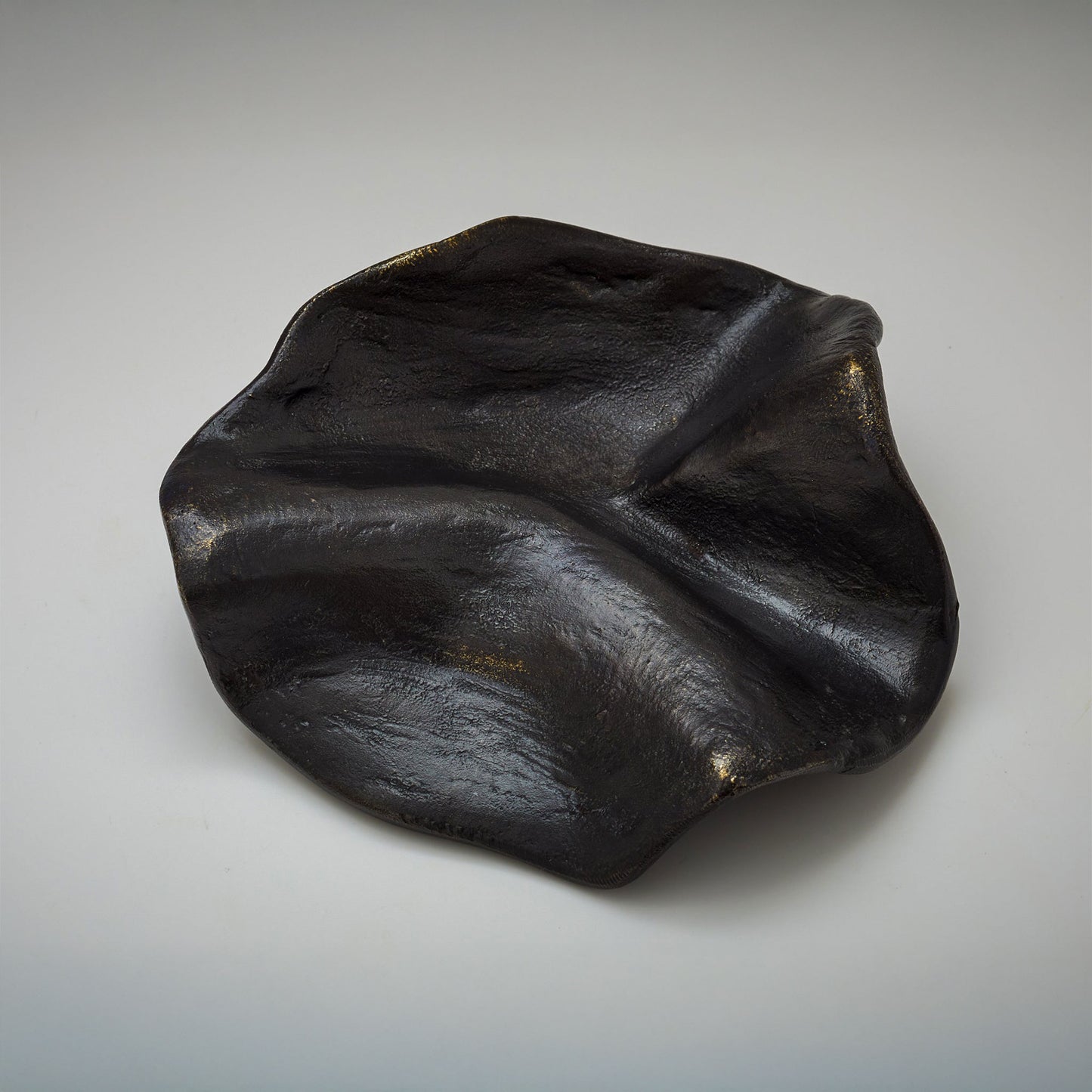 An organic-shaped metallic cabinet pull with a highly reflective, textured surface, photographed on a neutral light gray background.