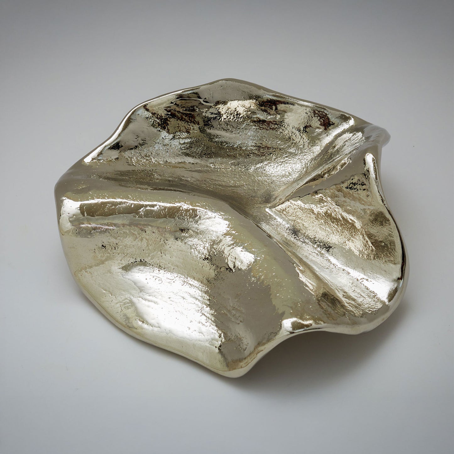 An organic-shaped metallic cabinet pull with a highly reflective, textured surface, photographed on a neutral light gray background.