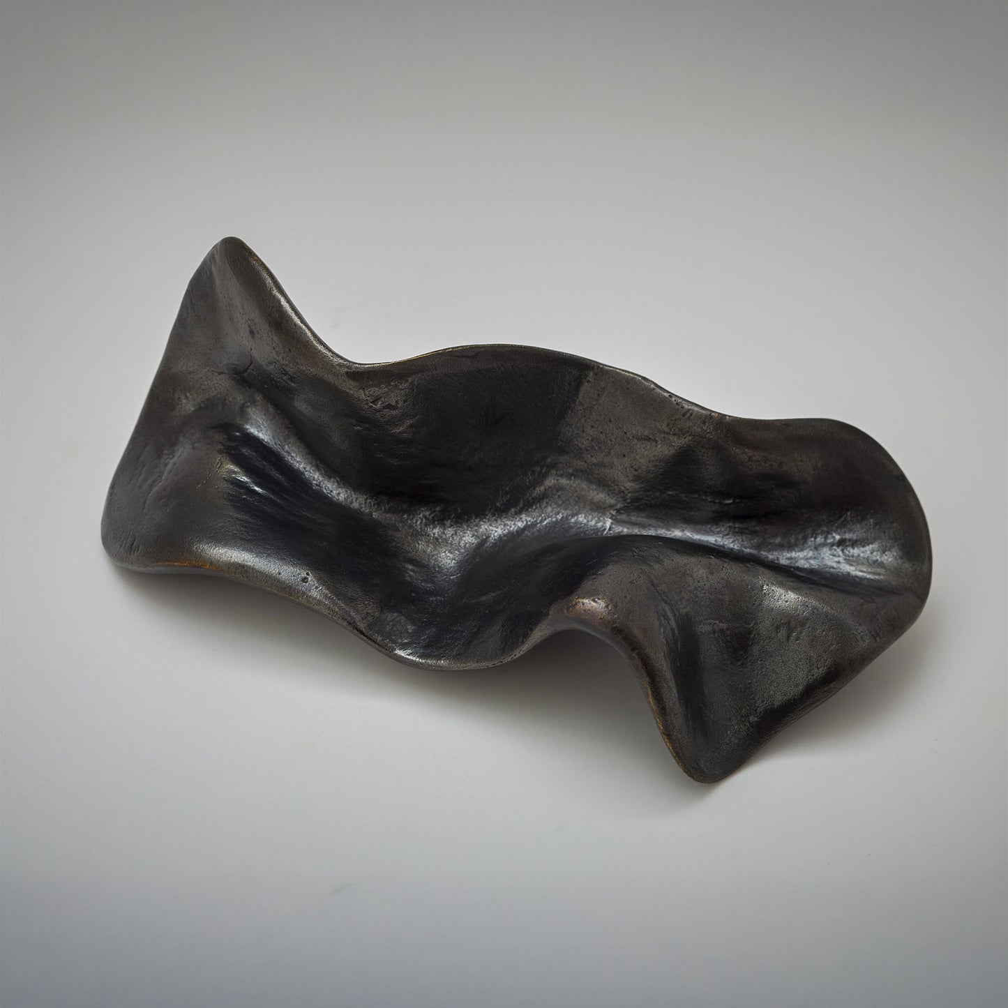 An abstract, fluid-shaped cabinet pull with a wavy, organic silhouette and a textured, reflective finish, photographed on a neutral light gray background.