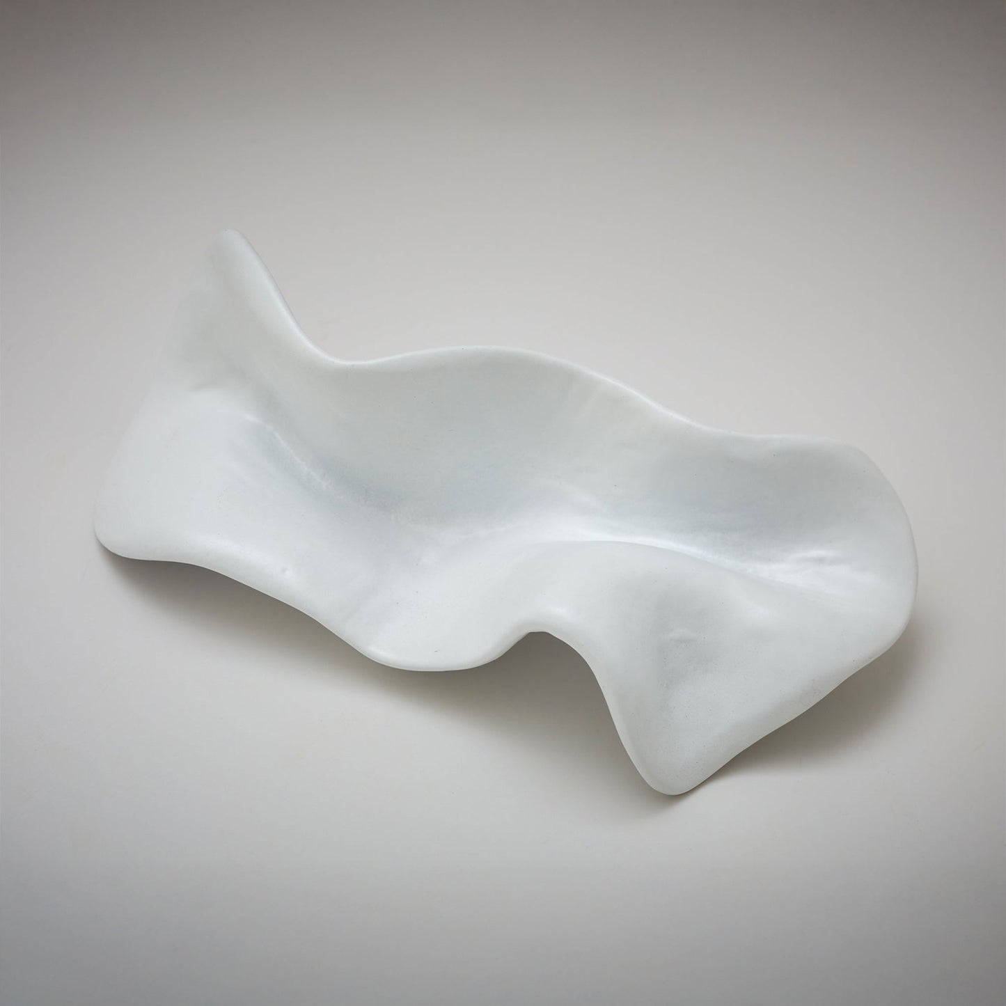 An abstract, fluid-shaped cabinet pull with a wavy, organic silhouette and a textured, reflective finish, photographed on a neutral light gray background.
