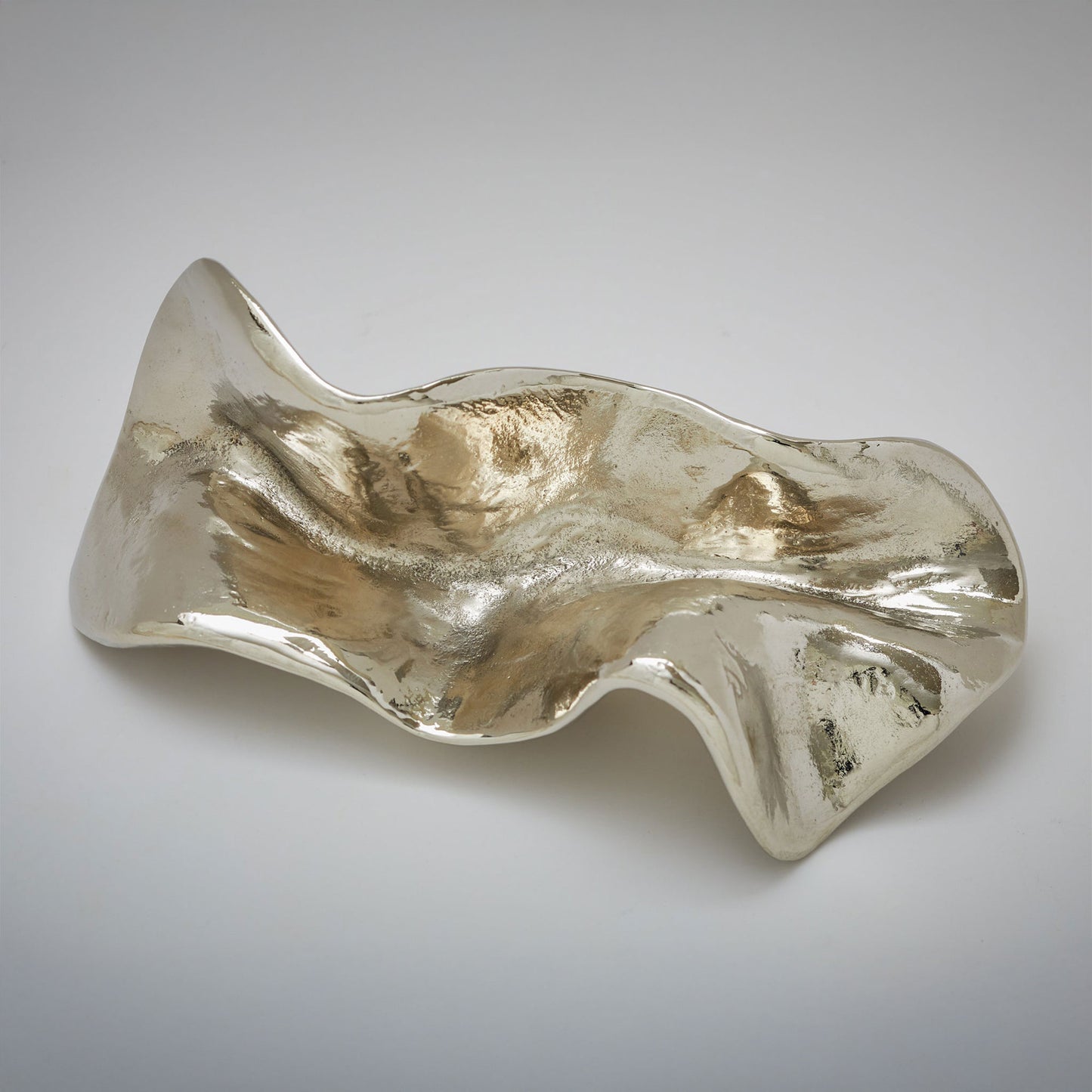 An abstract, fluid-shaped cabinet pull with a wavy, organic silhouette and a textured, reflective finish, photographed on a neutral light gray background.