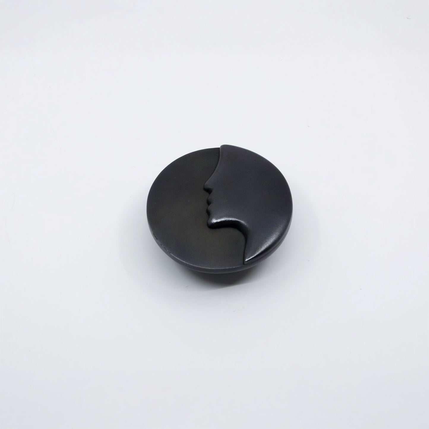 A round black cabinet knob with a small cutout detail, shown on a plain white background.