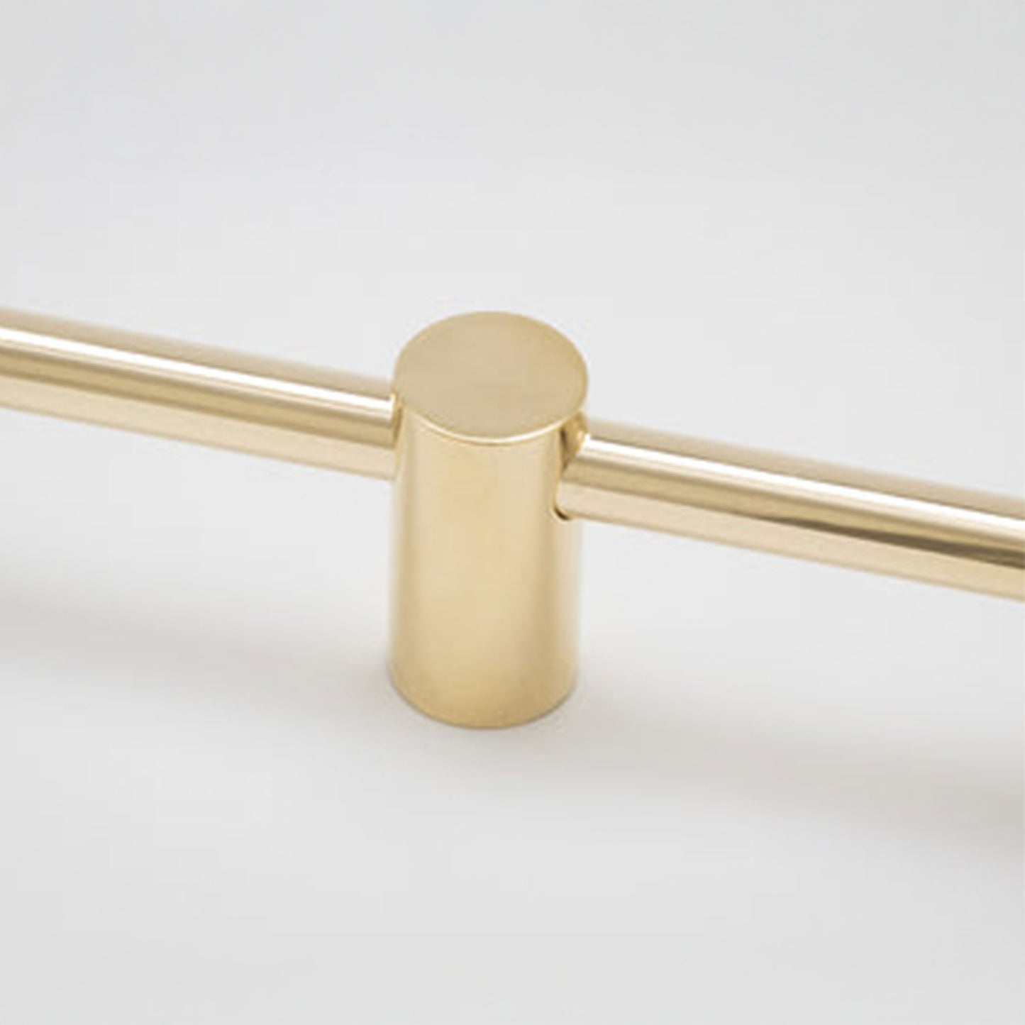A close-up of a brushed brass or gold-finished metal hardware piece, showing a cylindrical post connected to two horizontal bars on a plain light background.
