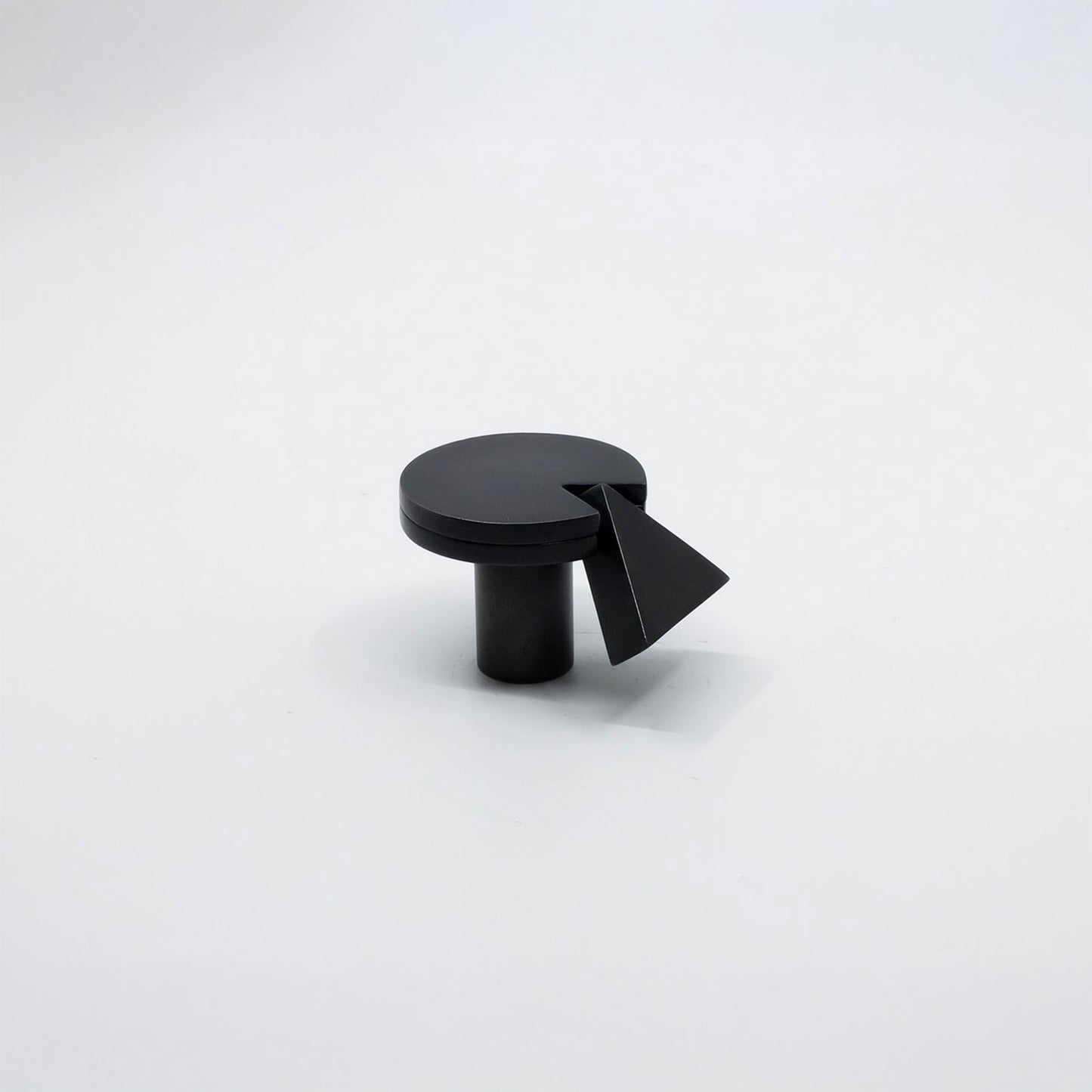 A matte black cabinet knob with a circular top and a triangular pull accent, shown on a clean white background.