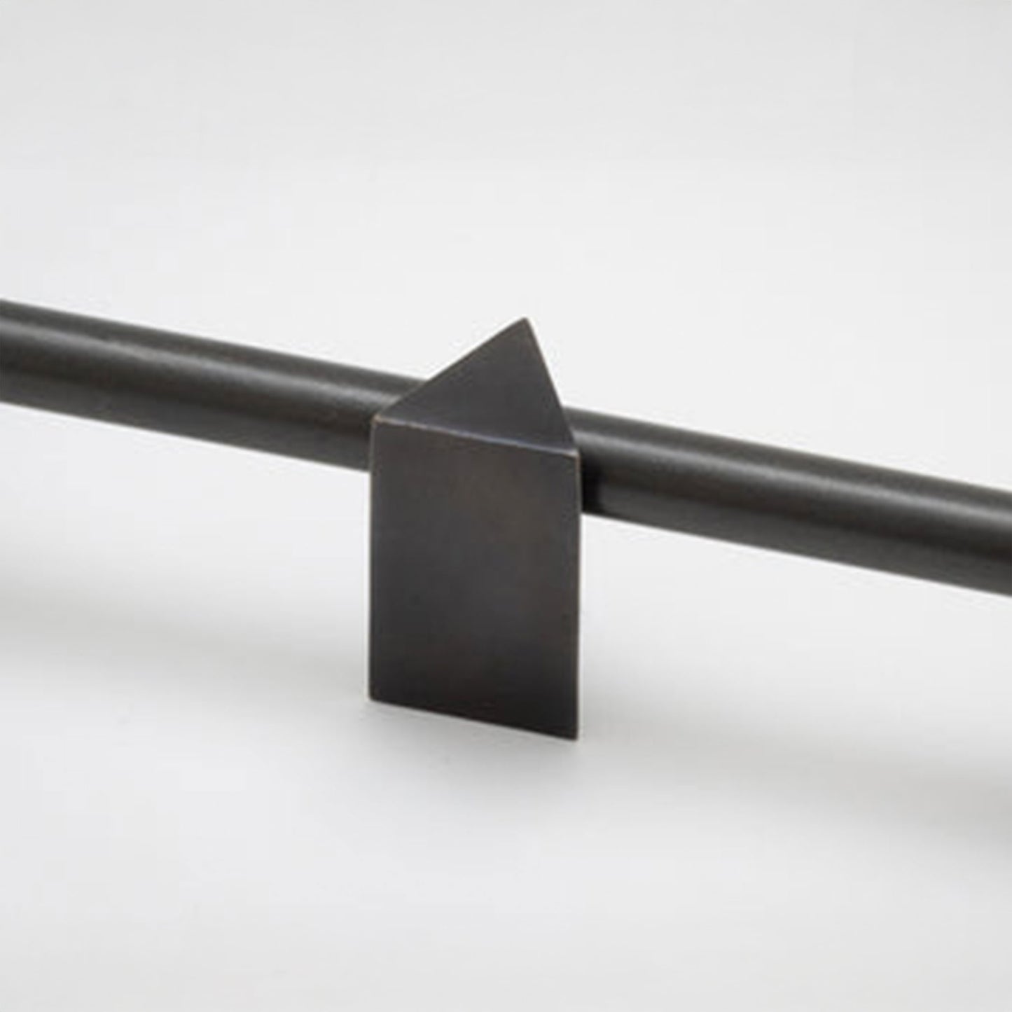 A close-up of a matte black metal cabinet knobs with a geometric triangular finial, shown against a clean light gray background.