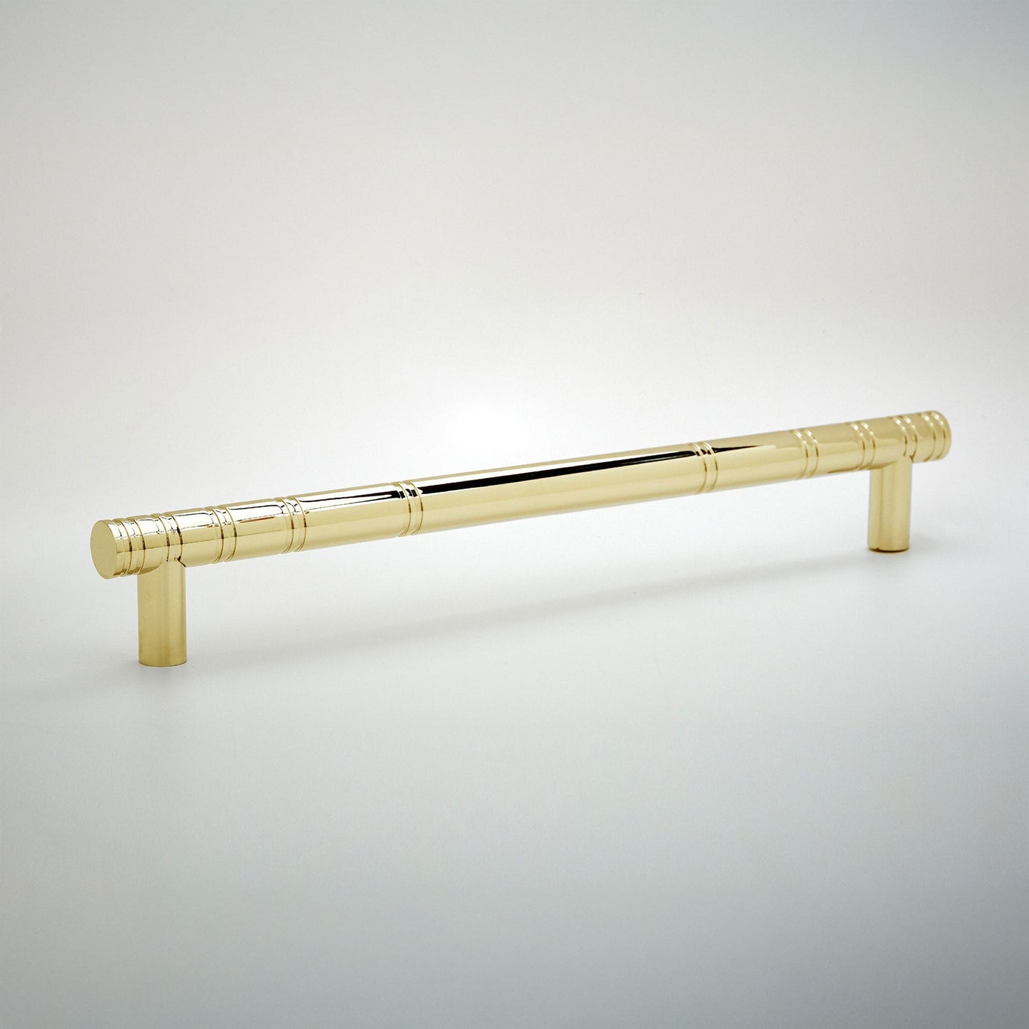 A polished brass cabinet pull handle with a decorative segmented rod design and cylindrical end caps, shown on a light gray gradient background.