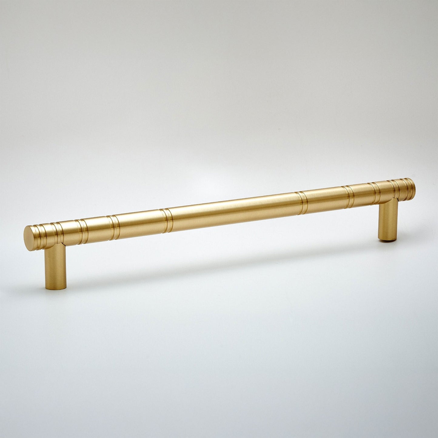 A brushed brass cabinet pull handle with a modern cylindrical design and subtle horizontal grooved accents, shown on a light gray background.
