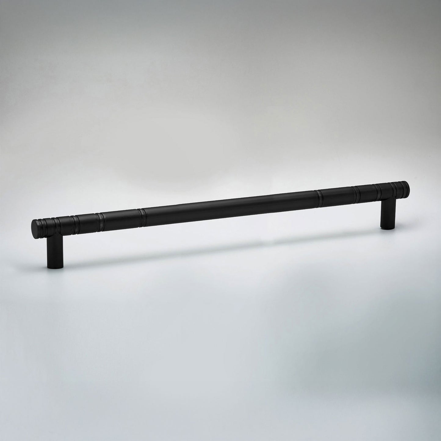 A long, black cabinet pull handle with a textured, segmented design and cylindrical end caps, shown on a light gray gradient background.