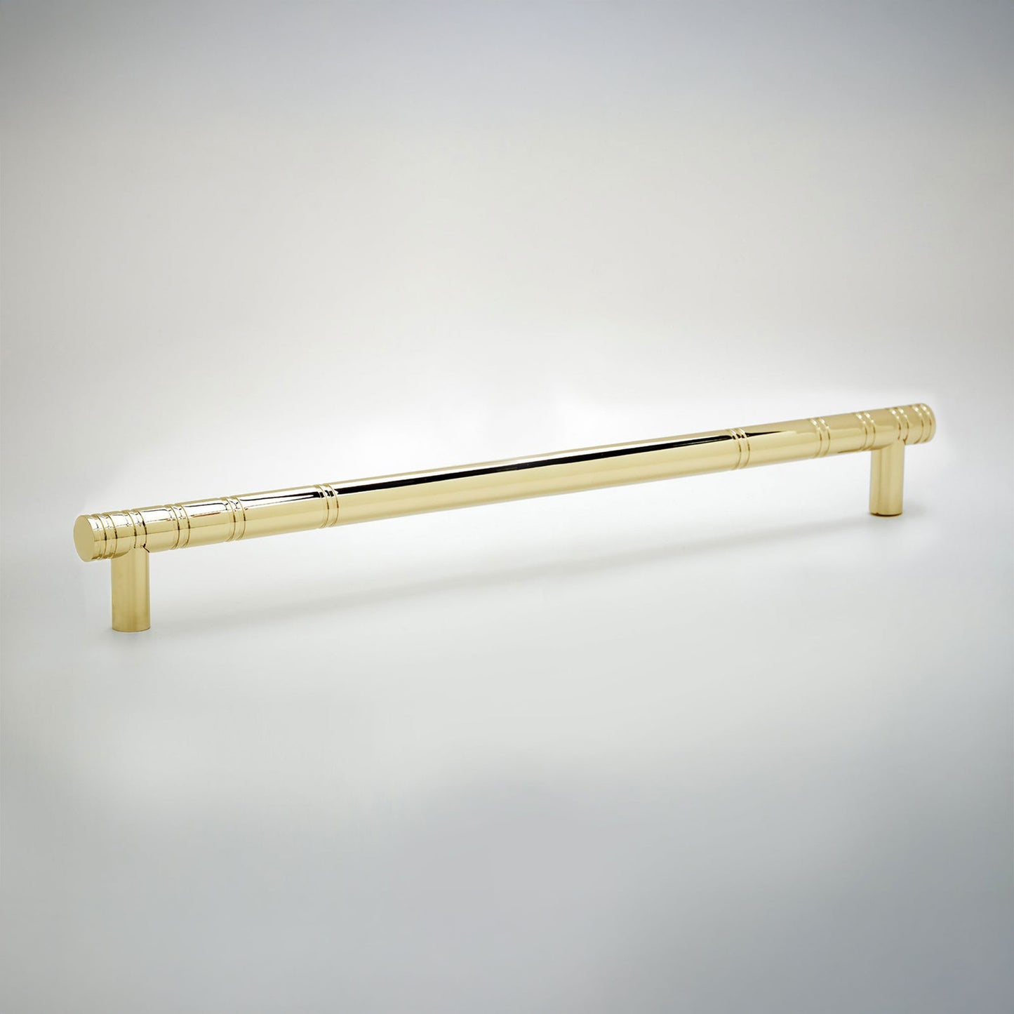 A polished brass cabinet pull handle with a modern cylindrical design and subtle horizontal grooved accents, shown on a light gray gradient background.