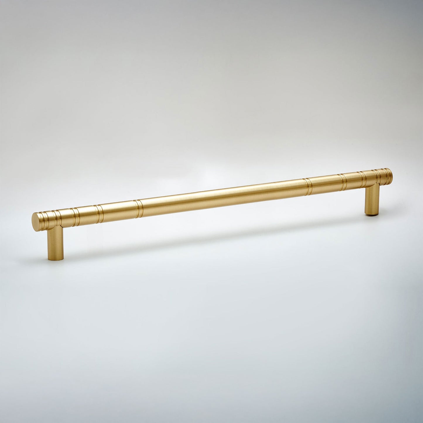 A modern cylindrical cabinet pull handle in a brushed gold finish, featuring a subtle textured pattern near the ends and mounting posts, shown on a neutral light gray background.