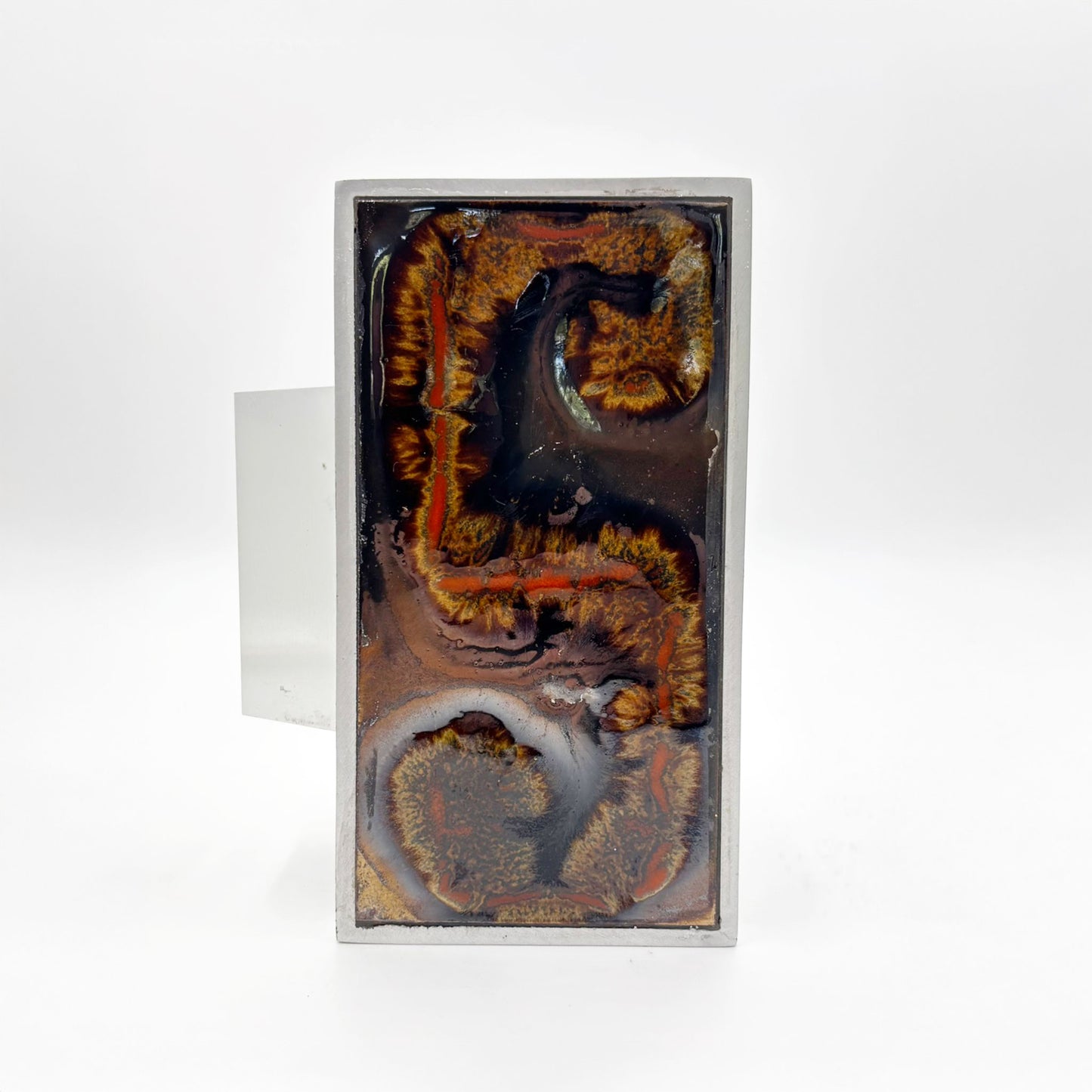 A single rectangular silver-toned door handles with abstract Orange, russet and tan textured inlay on a dark background, shown against a plain white background.