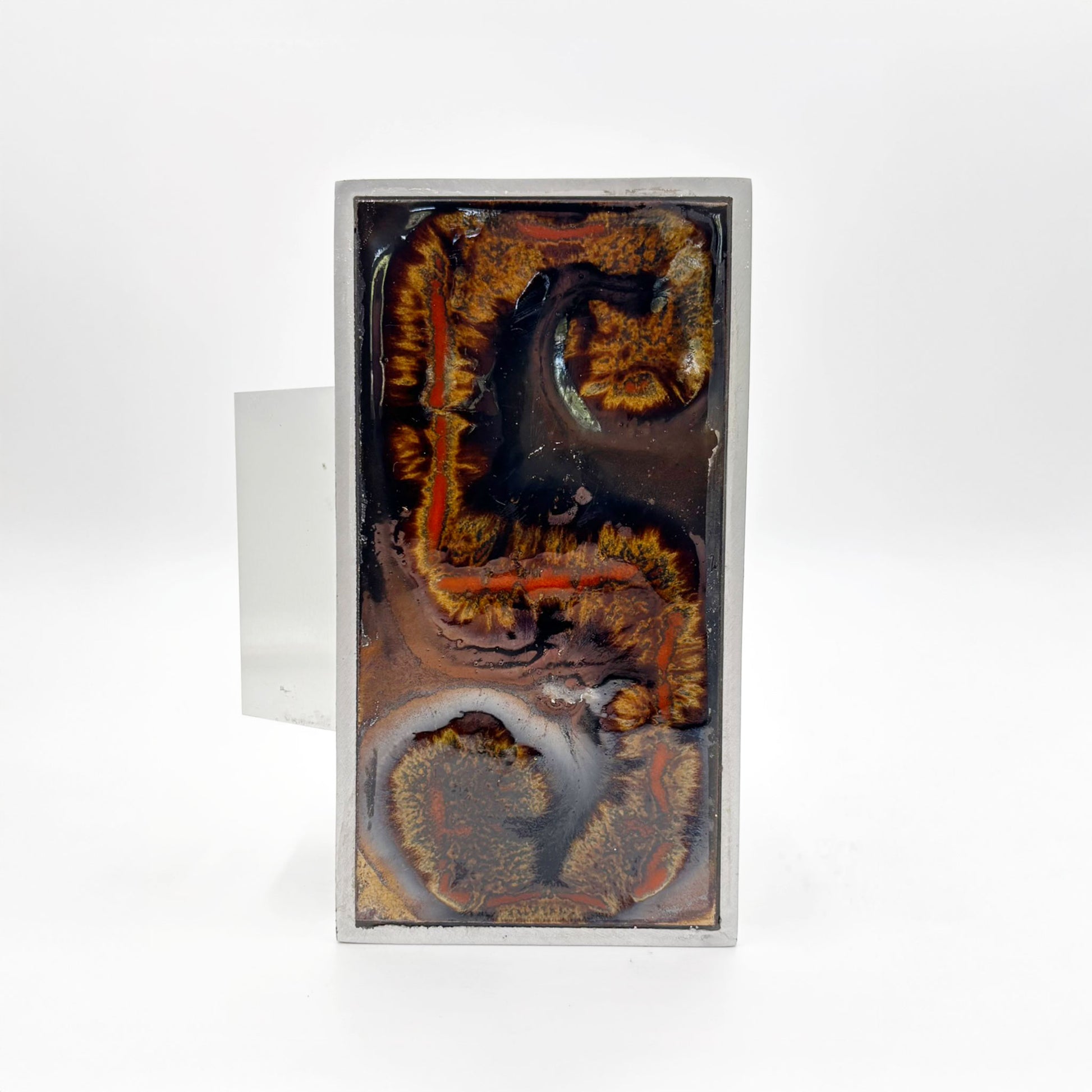 A single rectangular silver-toned door handles with abstract Orange, russet and tan textured inlay on a dark background, shown against a plain white background.