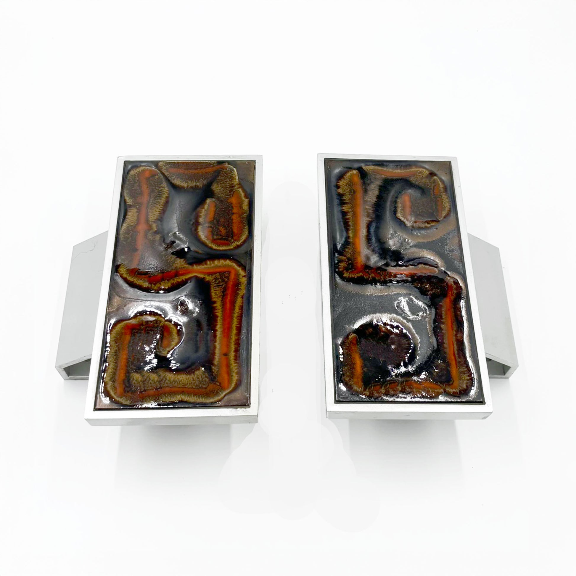 A pair of rectangular silver-toned door handles with abstract Orange, russet and tan textured inlay on a dark background, shown against a plain white background.