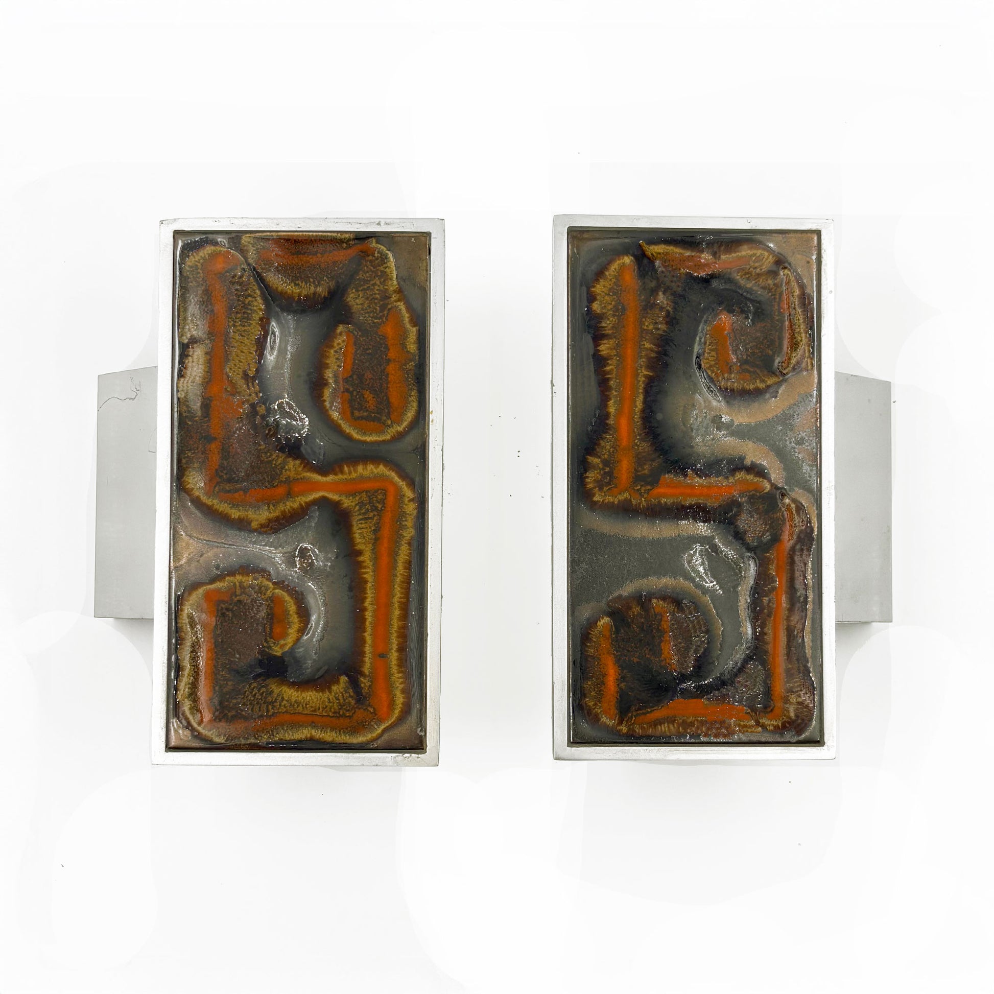 A pair of rectangular silver-toned door handles with abstract Orange, russet and tan textured inlay on a dark background, shown against a plain white background.