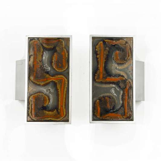 A pair of rectangular silver-toned door handles with abstract Orange, russet and tan textured inlay on a dark background, shown against a plain white background.