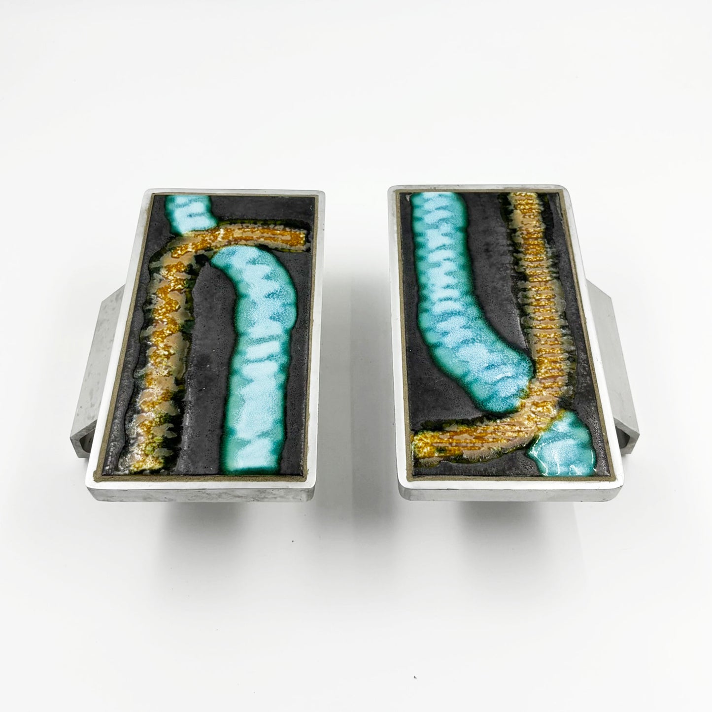 A pair of rectangular silver-toned door handles with abstract turquoise and gold textured inlay on a dark background, shown against a plain white background.