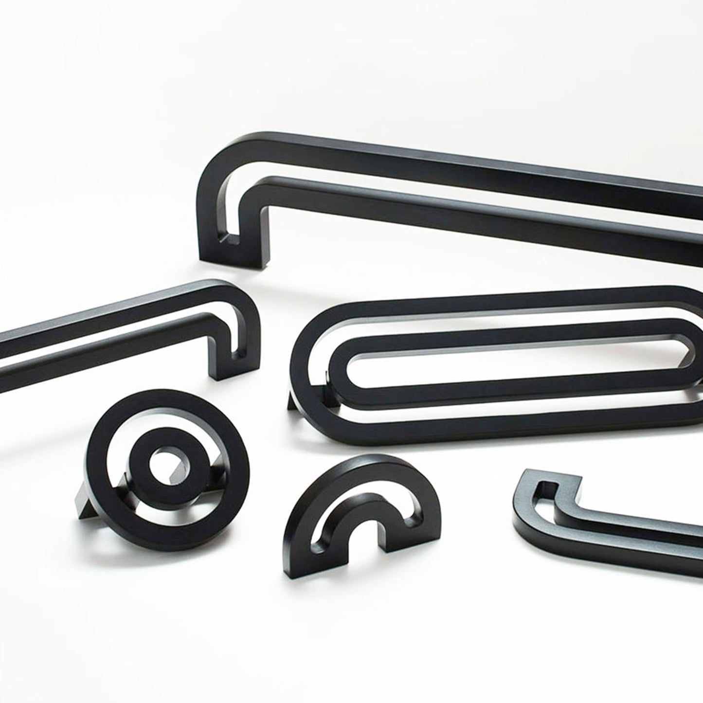 A set of matte black modern metal cabinet handles in various shapes, including double bars, an oval with a loop, a spiral, a semi-circular arch, and a curved hook, arranged on a clean white background.
