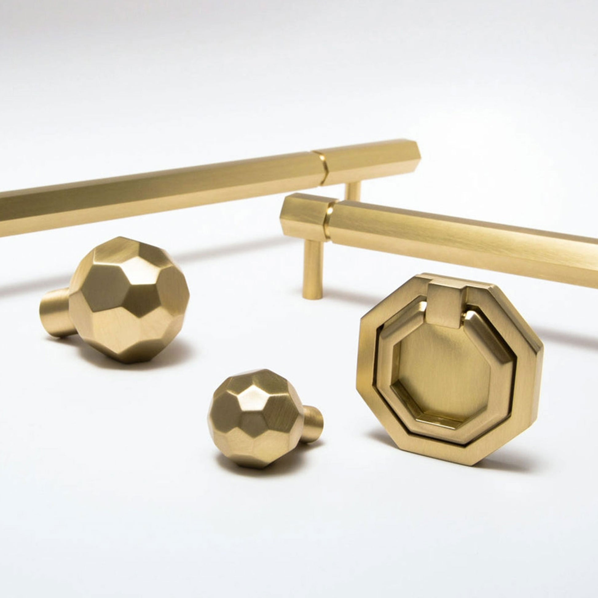 A set of modern brass hardware pieces, including two linear cabinet pulls, two faceted round knobs, and an octagonal ring pull, displayed on a clean white background.