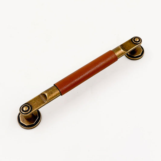 a bronze cabinet pull with a cognac colored leather handle on a white background