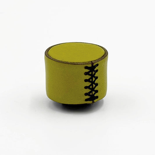 A small cylindrical cabinet knob in a muted olive-yellow color, styled like a miniature doll's head with black faux-stitch details down the front, set against a plain white background.