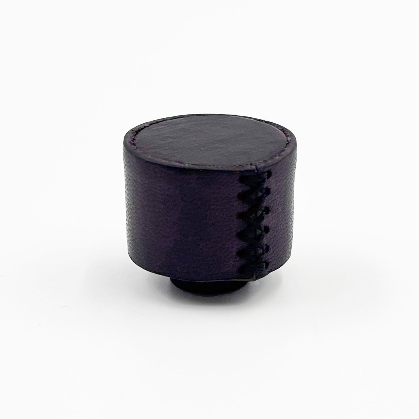 A small cylindrical dark purple cabinet  knob with decorative zigzag stitching on the side, photographed on a clean white background.