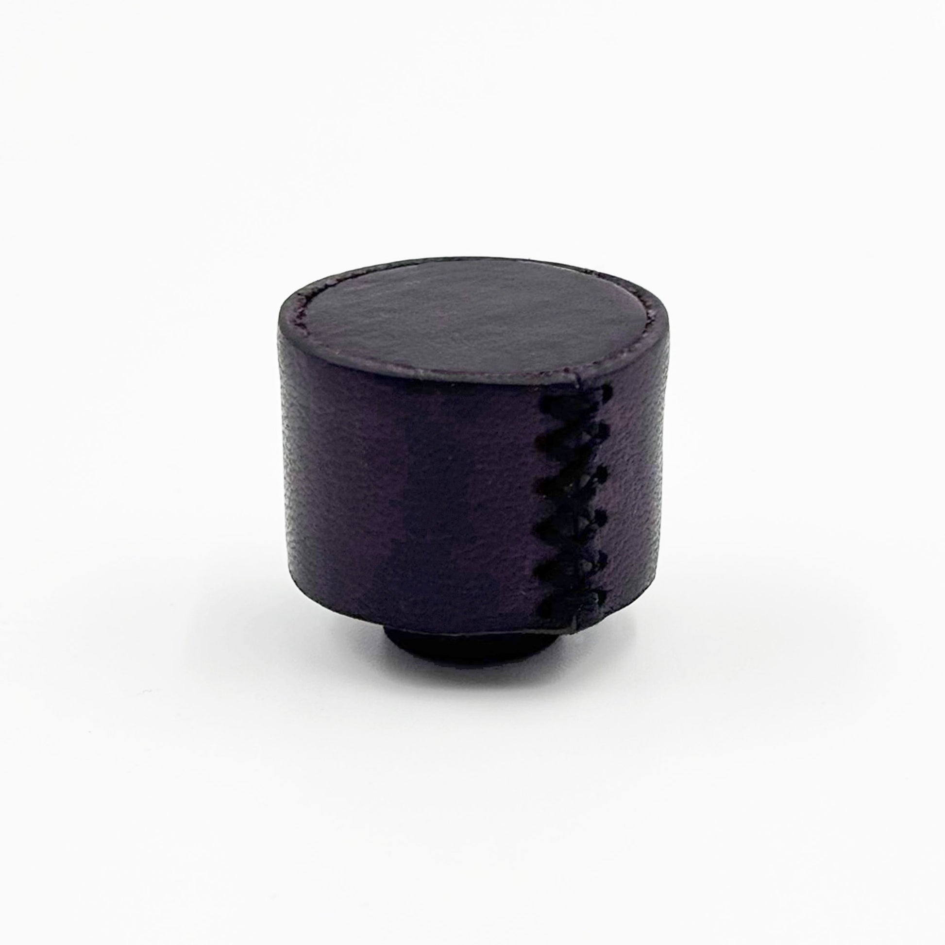 A small cylindrical dark purple cabinet  knob with decorative zigzag stitching on the side, photographed on a clean white background.