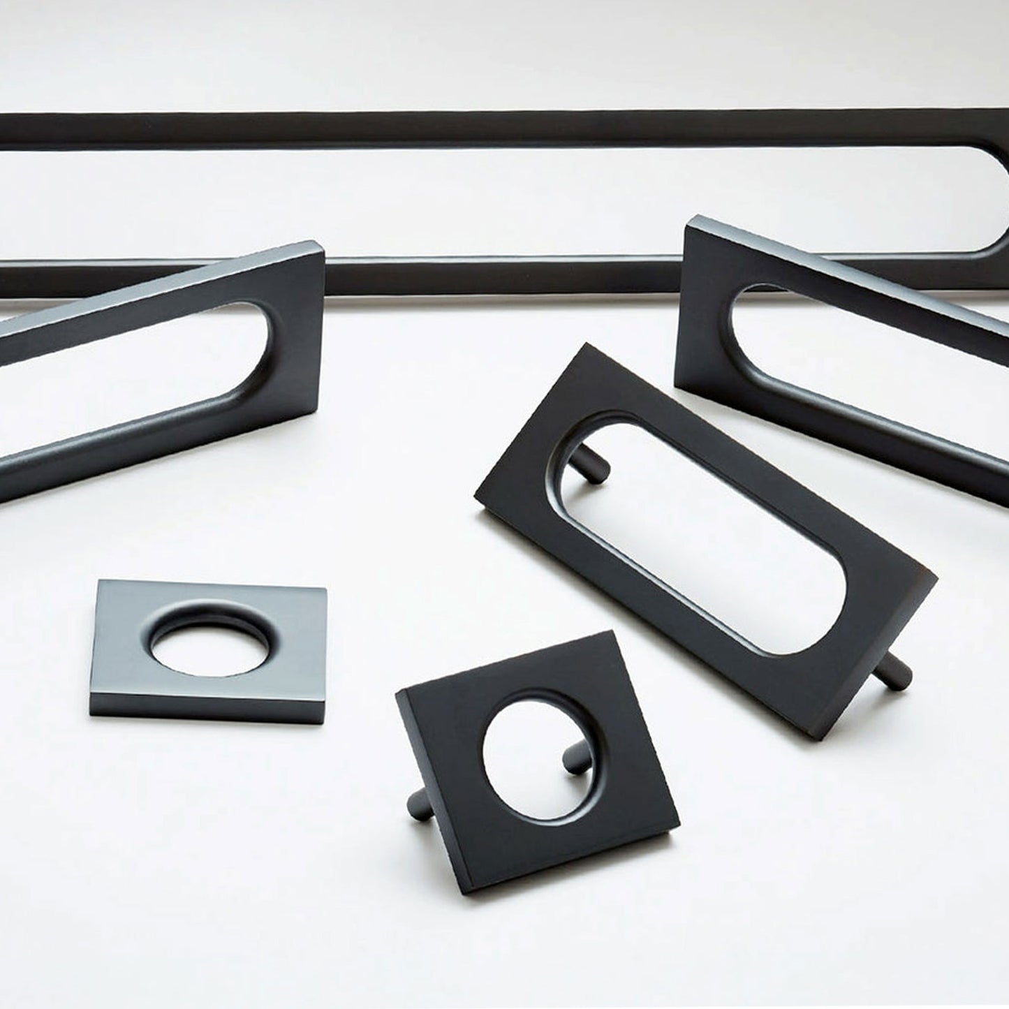 A set of matte black metal cabinet hardware, including rectangular and square pull handles with oval cutouts, arranged on a clean white background.