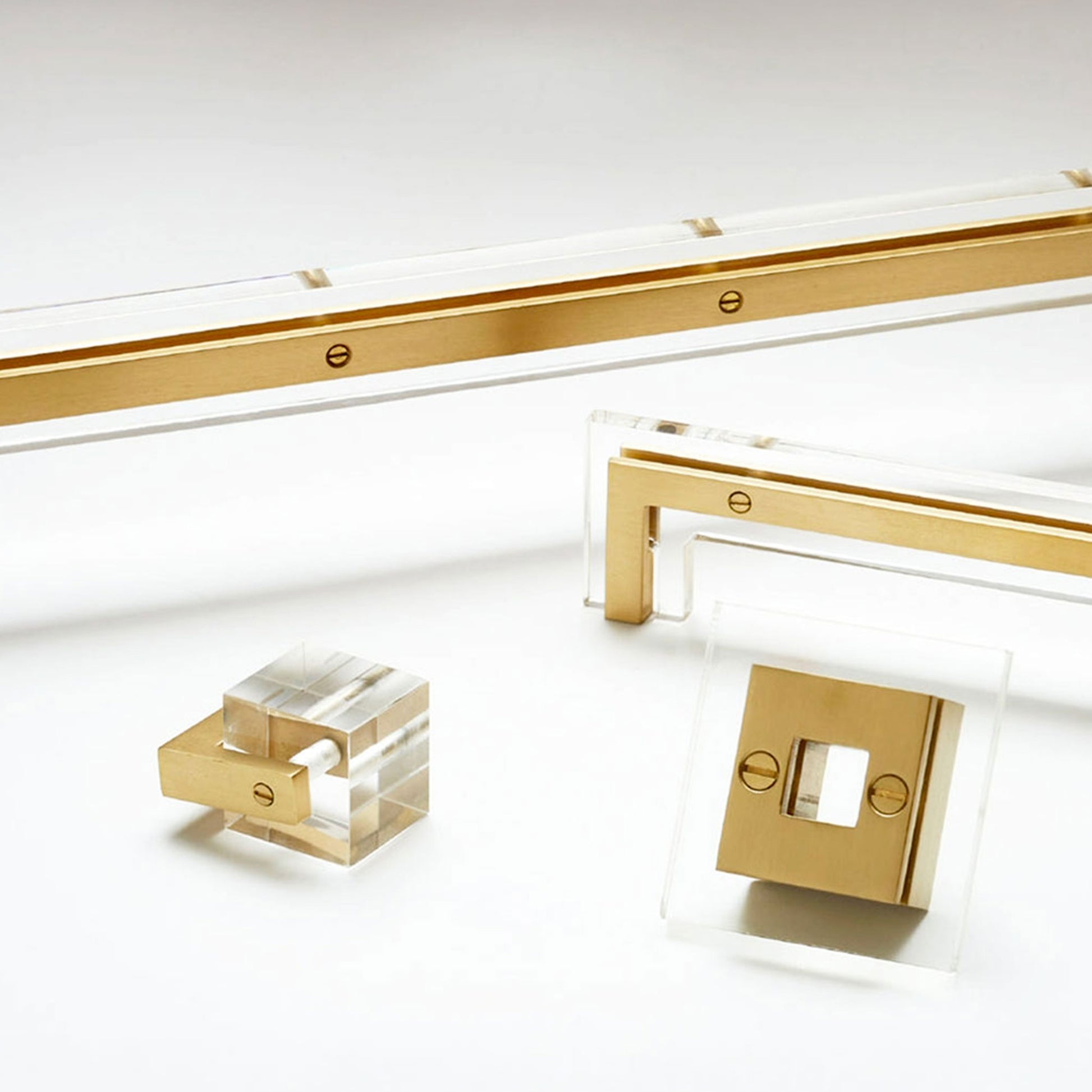 Gold-finished hardware components and clear acrylic blocks arranged on a clean white studio background.