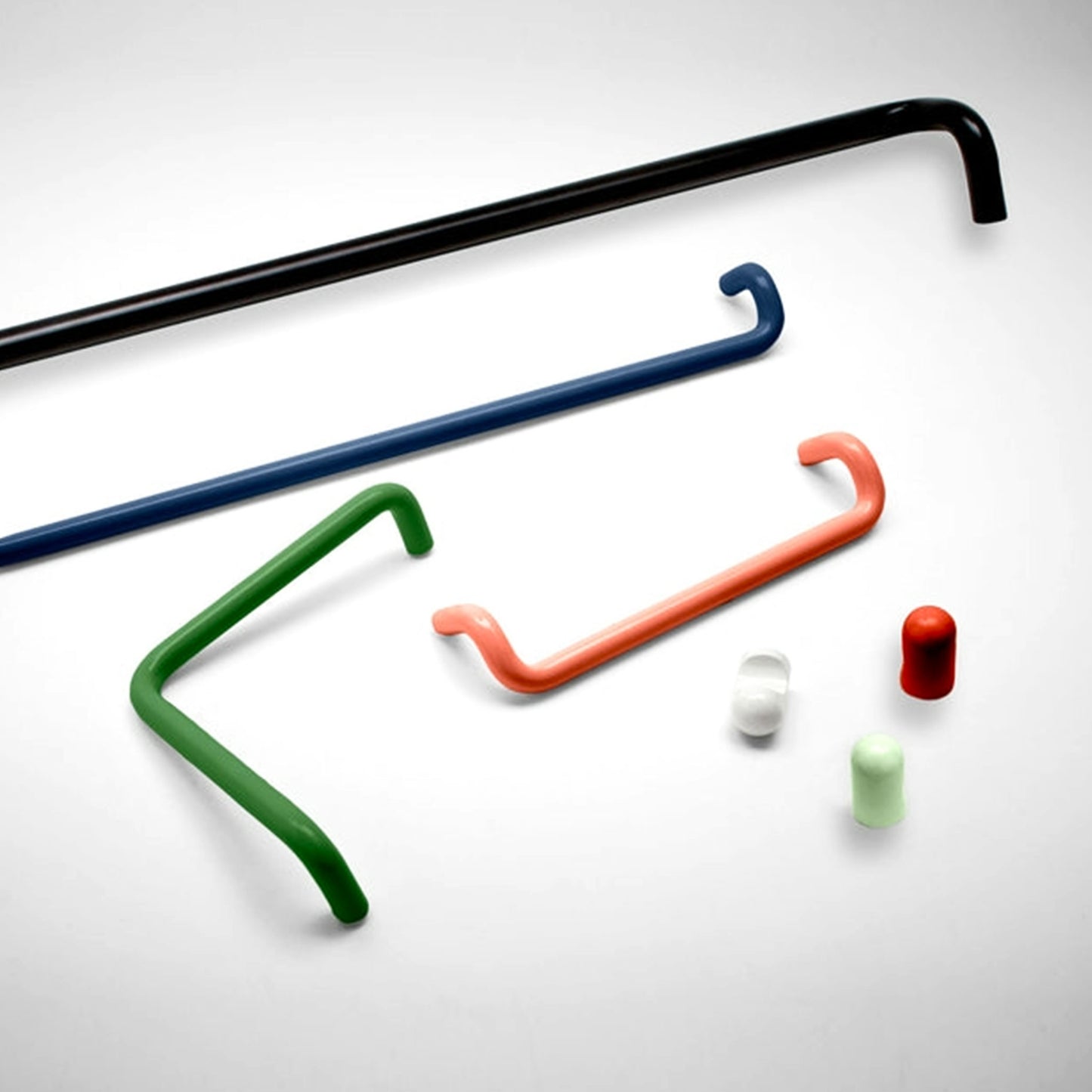 A set of modern minimalist cabinet pulls in black, blue, green, and orange, shown with small white and light green cylindrical caps on a light gray background.