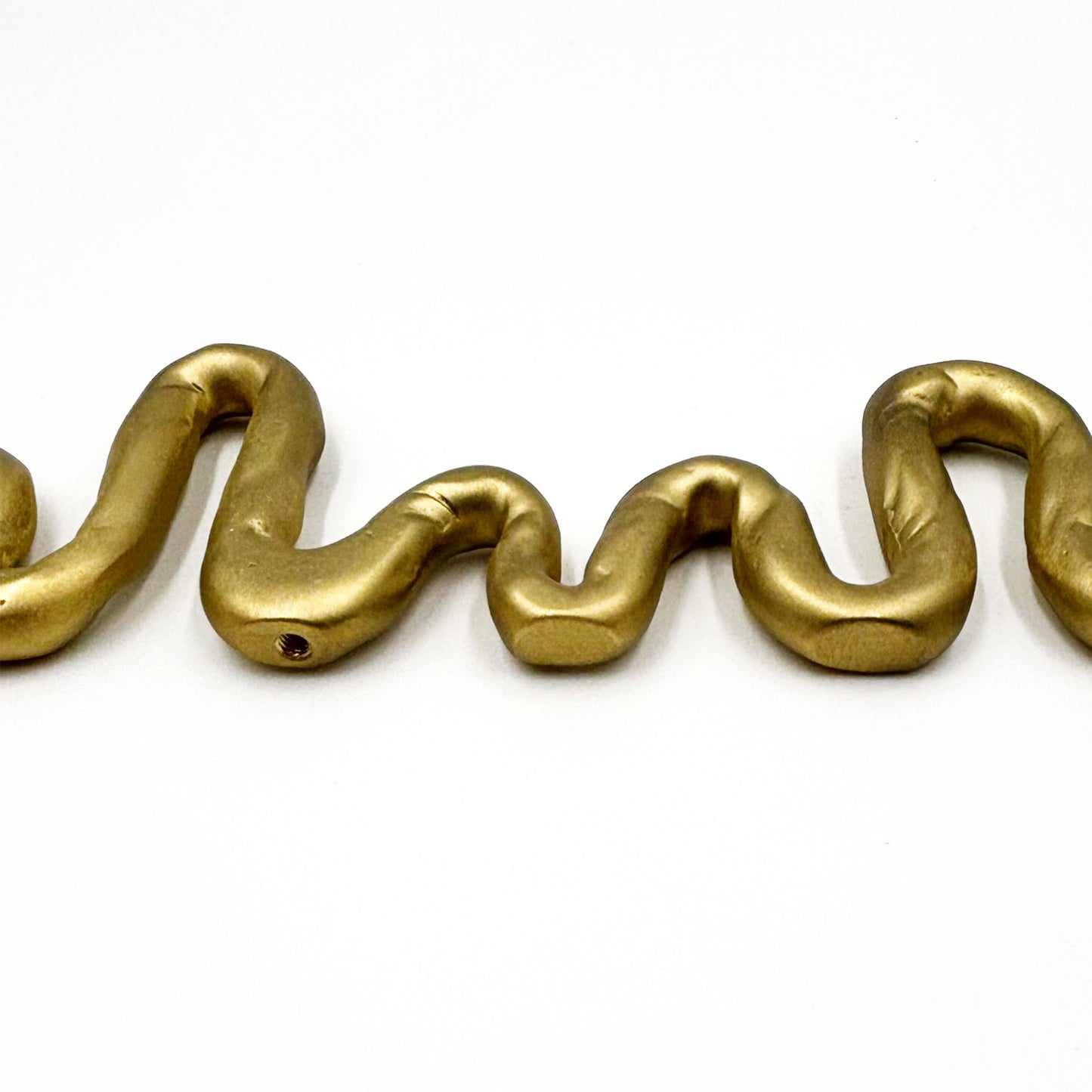 A close-up of A squiggly snake shaped matte brass colored cabinet pull in a white background