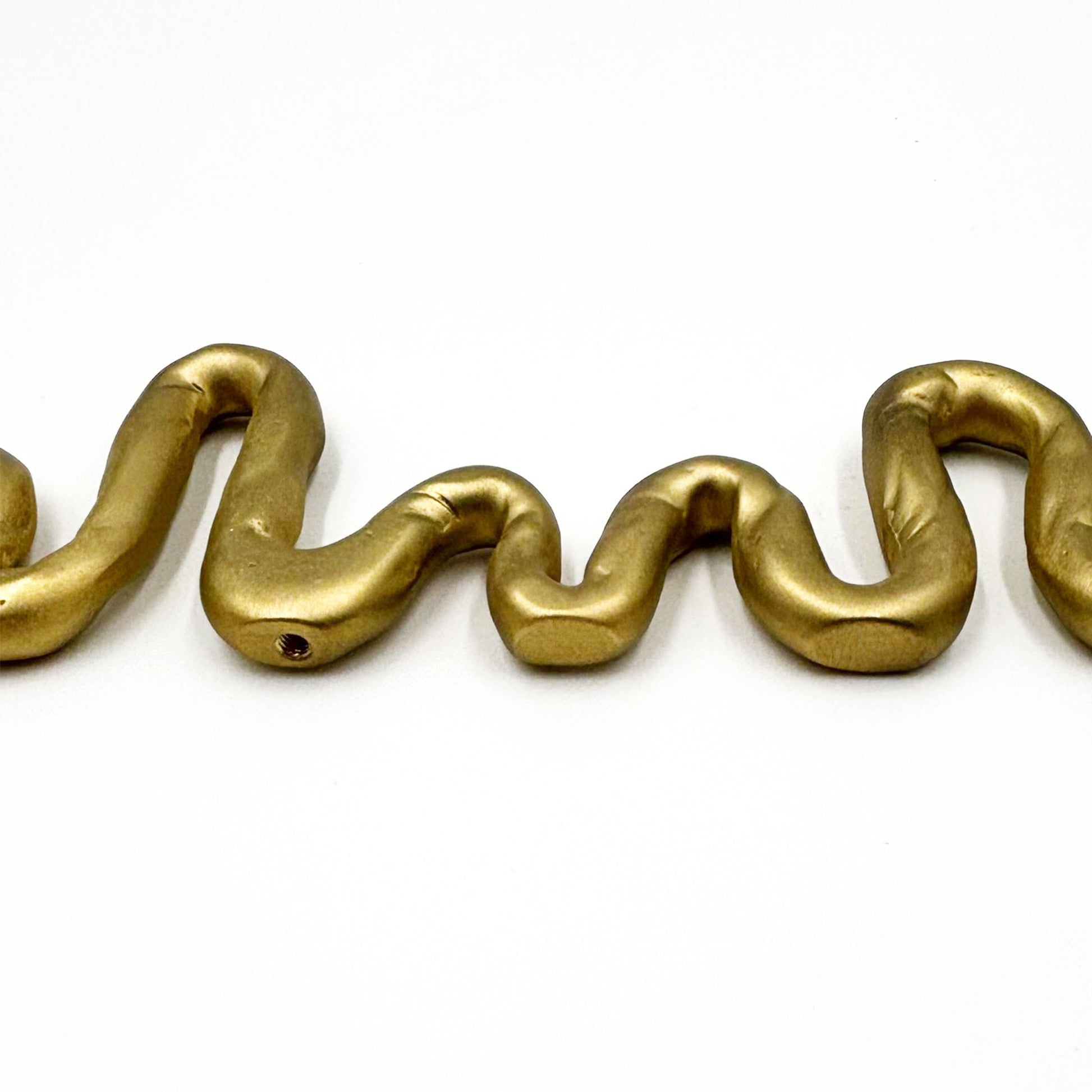 A close-up of A squiggly snake shaped matte brass colored cabinet pull in a white background