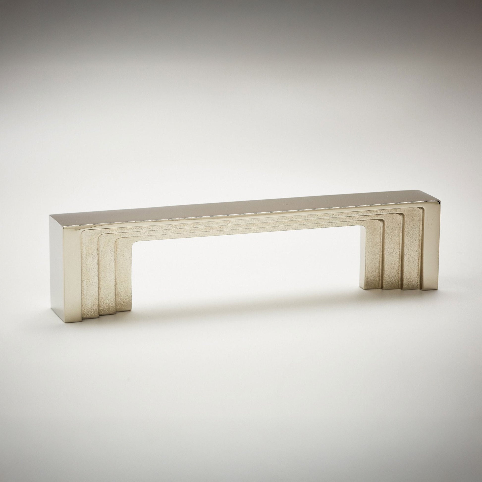 A modern rectangular cabinet pull handle with a brushed silver finish, featuring a stepped geometric design and a hollow center, shown on a light gray gradient background.