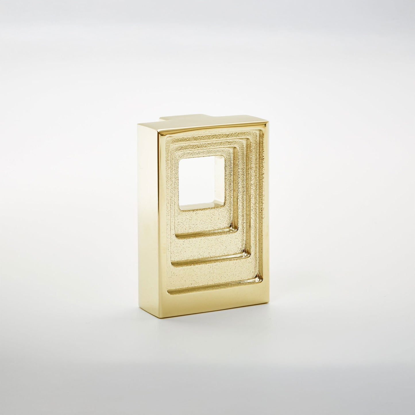A small rectangular gold-toned cabinet pull with a recessed square cutout, photographed on a clean light gray studio background.