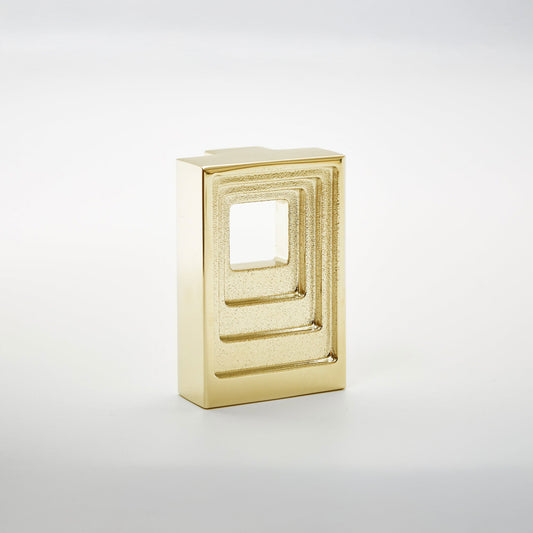 A small rectangular gold-toned cabinet pull with a recessed square cutout, photographed on a clean light gray studio background.