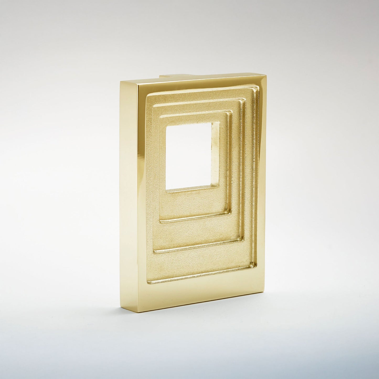A modern, minimalist gold-toned geometric cabinet pull featuring a series of nested rectangular frames with a central square cutout, set against a clean light gray gradient background.