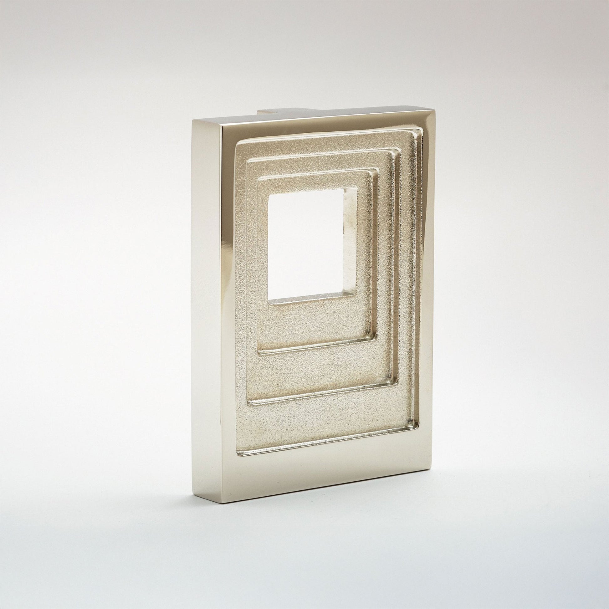 A modern rectangular cabinet pull  with a metallic silver finish and a nested square window design, photographed on a seamless light gray background.
