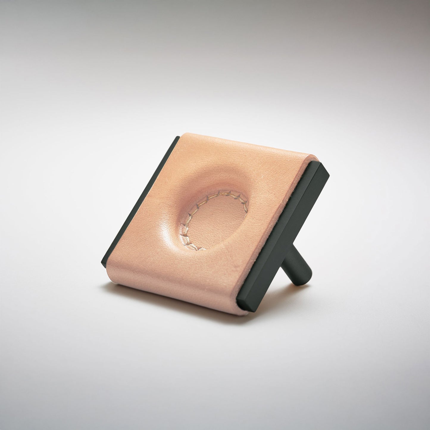 A light leather and metal square cabinet knob on a clean greay background