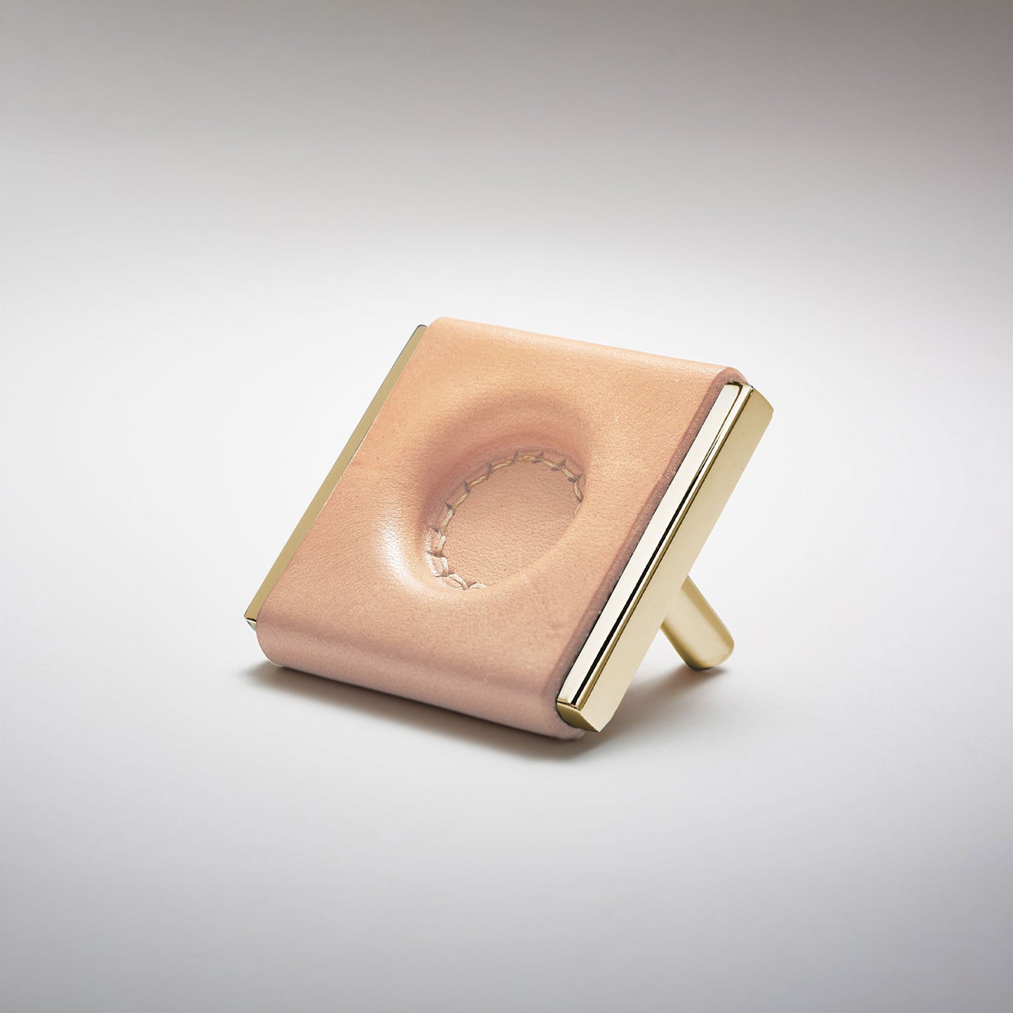 A light leather and metal square cabinet knob on a clean greay background