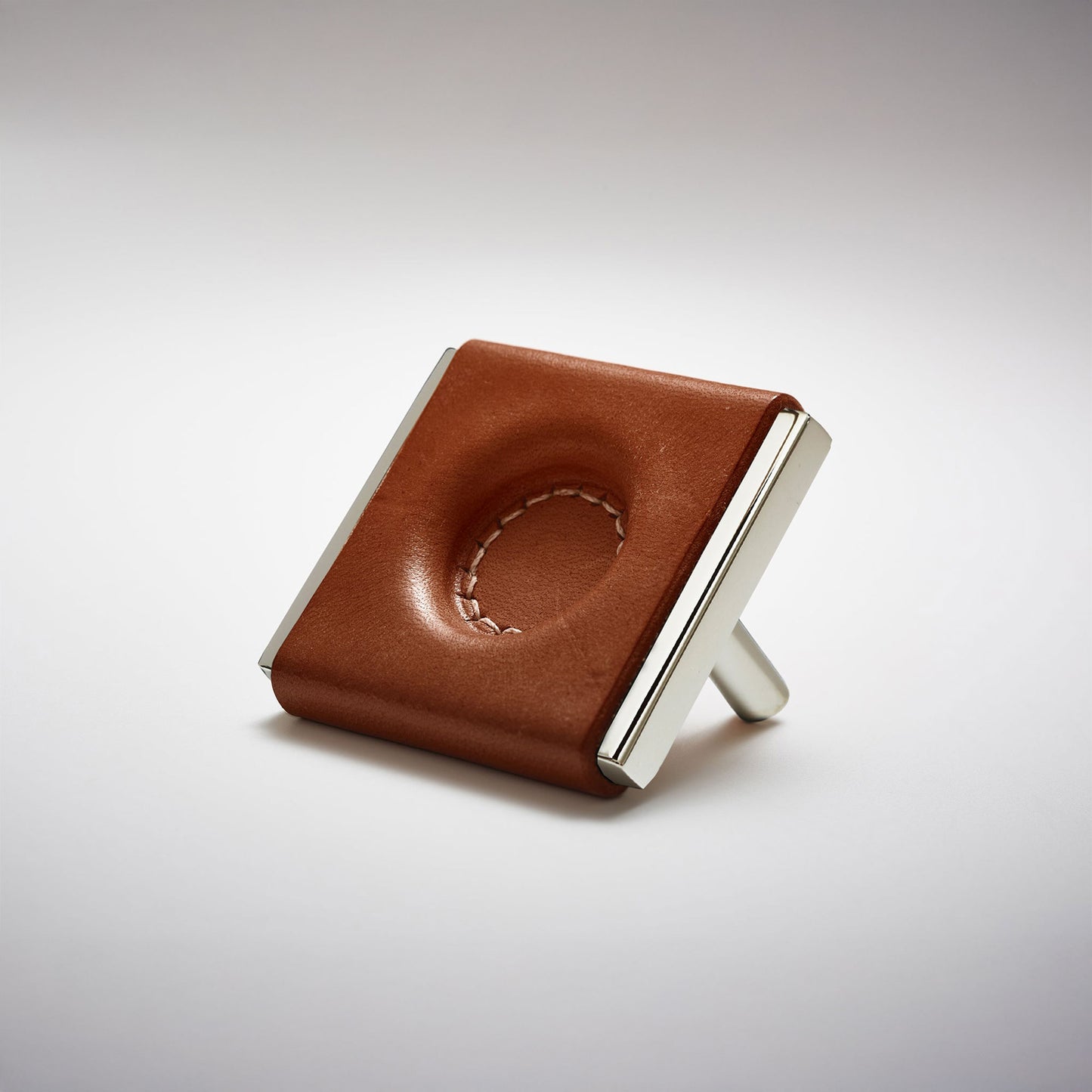 A dark leather and metal square cabinet knob on a clean greay background