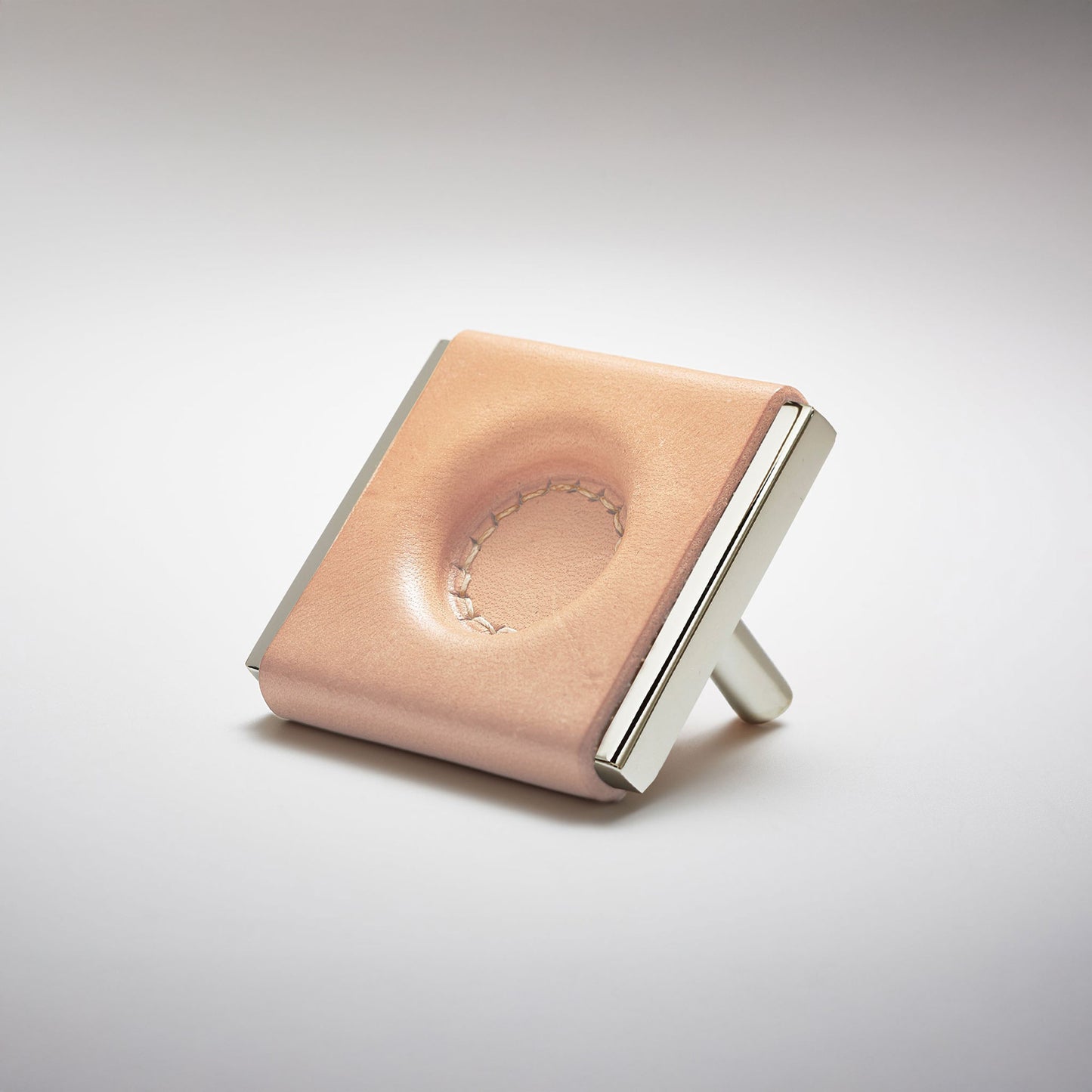 A light leather and metal square cabinet knob on a clean greay background