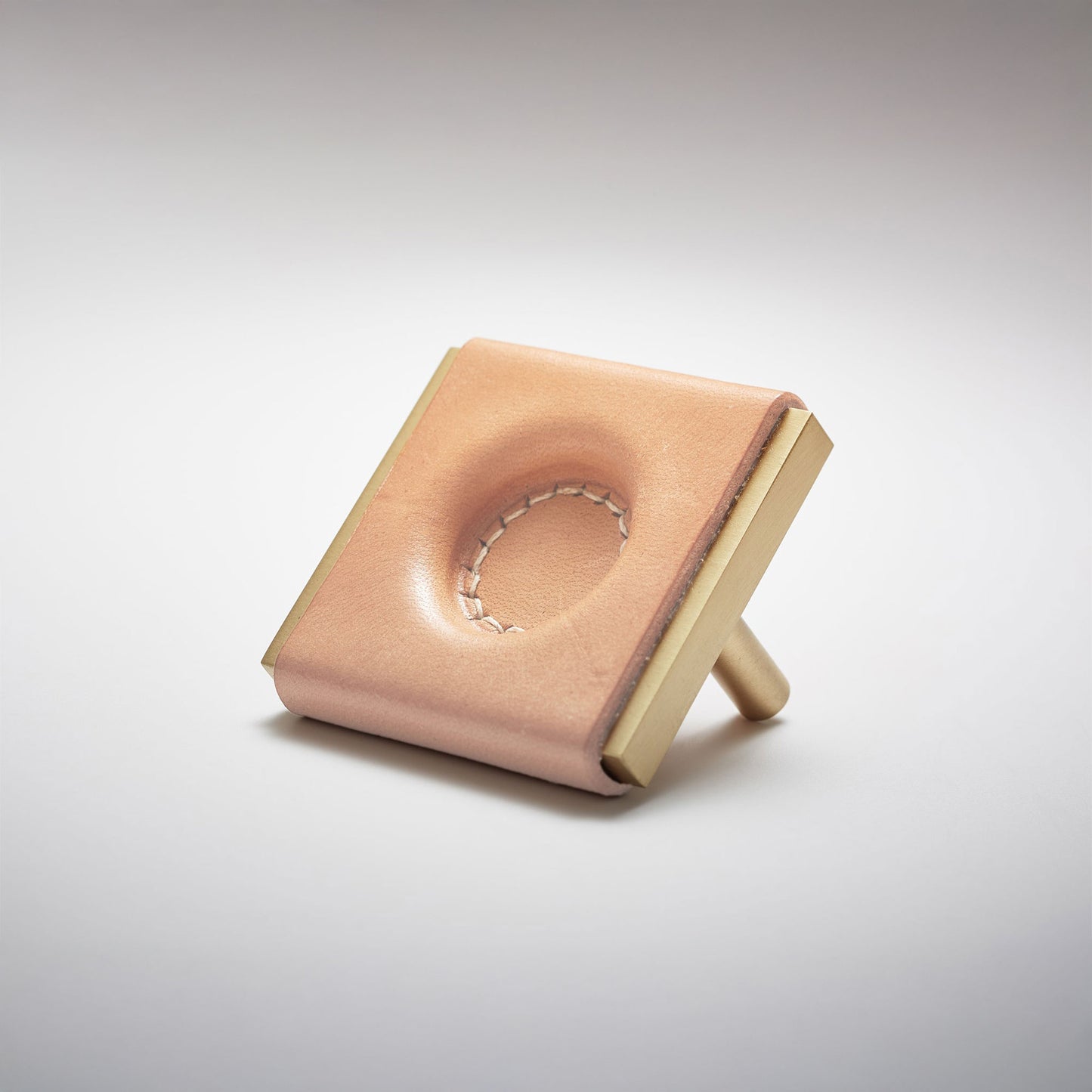 A light leather and metal square cabinet knob on a clean greay background