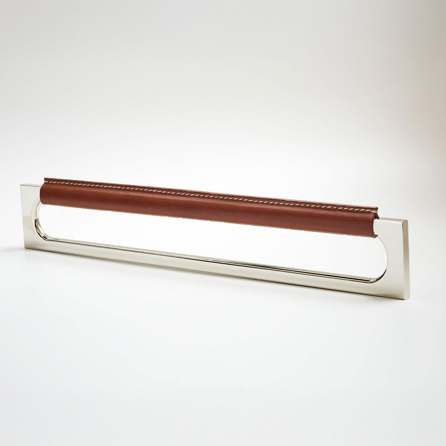 A modern rectangular metal cabinet pull with a central cutout, featuring a light brown leather strap stitched across the top, shown on a clean grey studio background.
