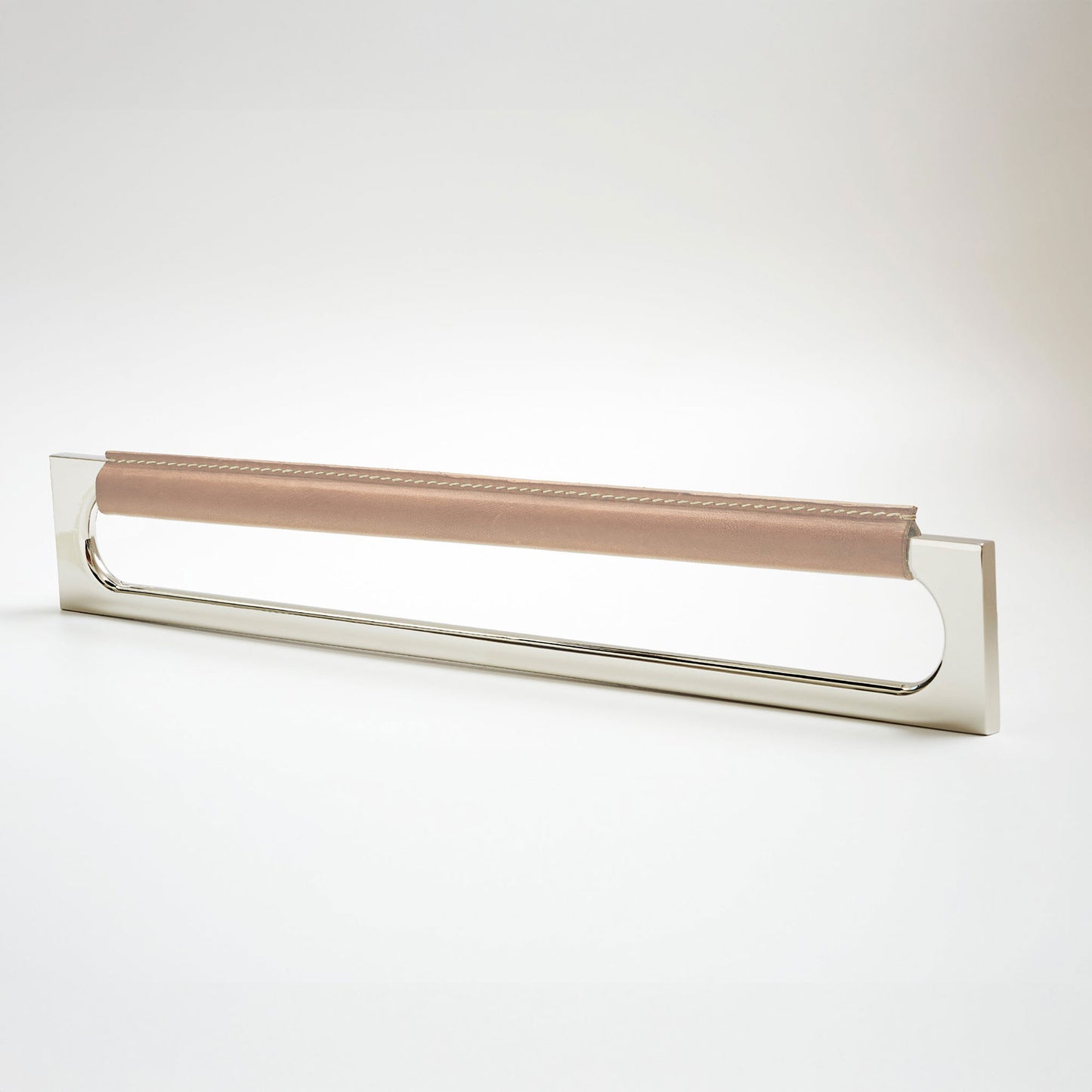 A modern rectangular metal cabinet pull with a central cutout, featuring a light tan leather strap stitched across the top, shown on a clean grey studio background.