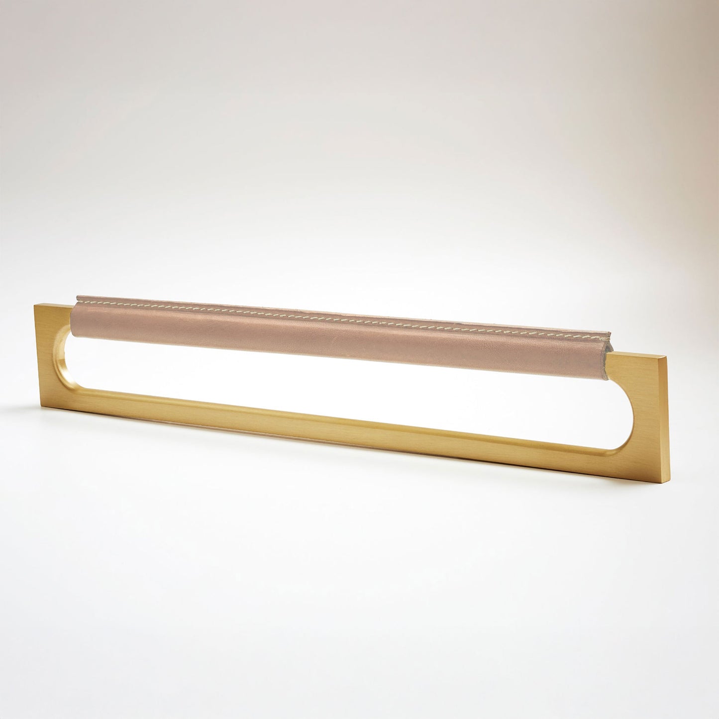 A modern rectangular metal cabinet pull with a central cutout, featuring a light tan leather strap stitched across the top, shown on a clean grey studio background.