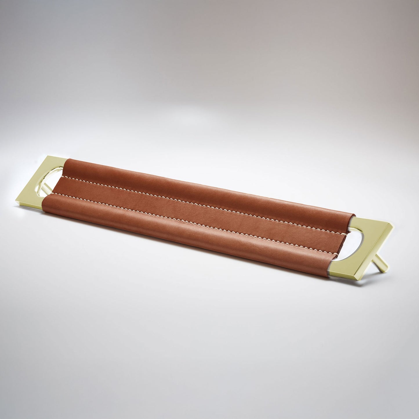 A modern rectangular metal cabinet pull with a central cutout, featuring a light brown leather strap stitched across the top, shown on a clean grey studio background.