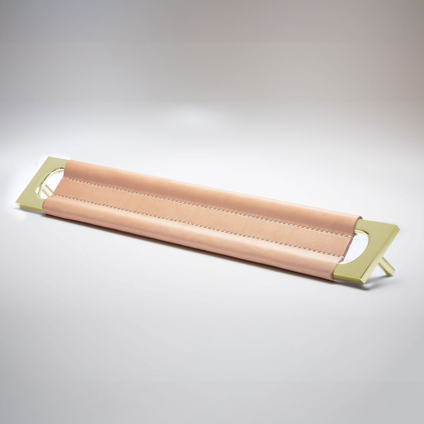 A modern rectangular metal cabinet pull with a central cutout, featuring a light tan leather strap stitched across the top, shown on a clean grey studio background.