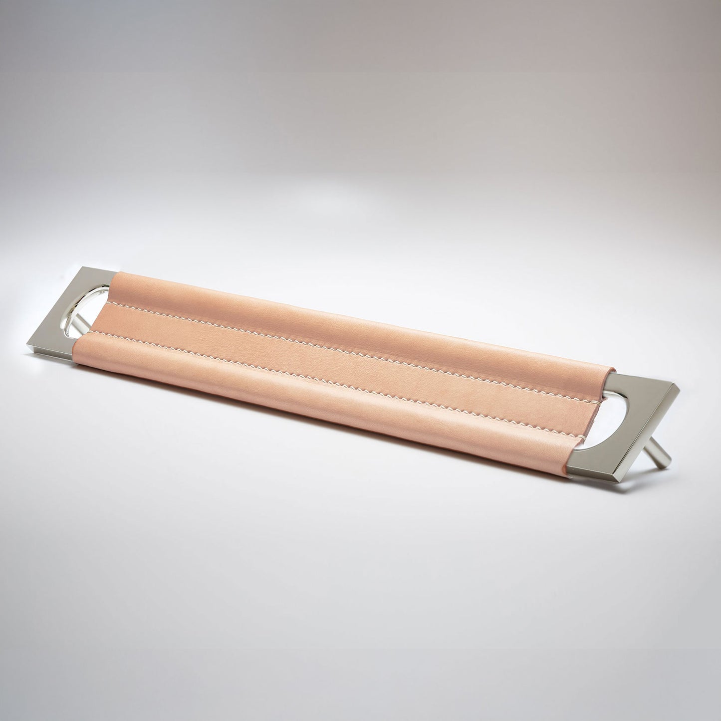 A modern rectangular metal cabinet pull with a central cutout, featuring a light tan leather strap stitched across the top, shown on a clean grey studio background.