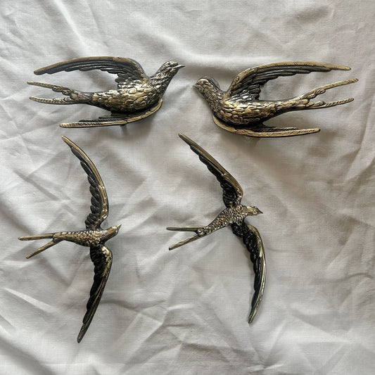 Four antique brass realistic bird shape cabinet pulls on a textured white surface