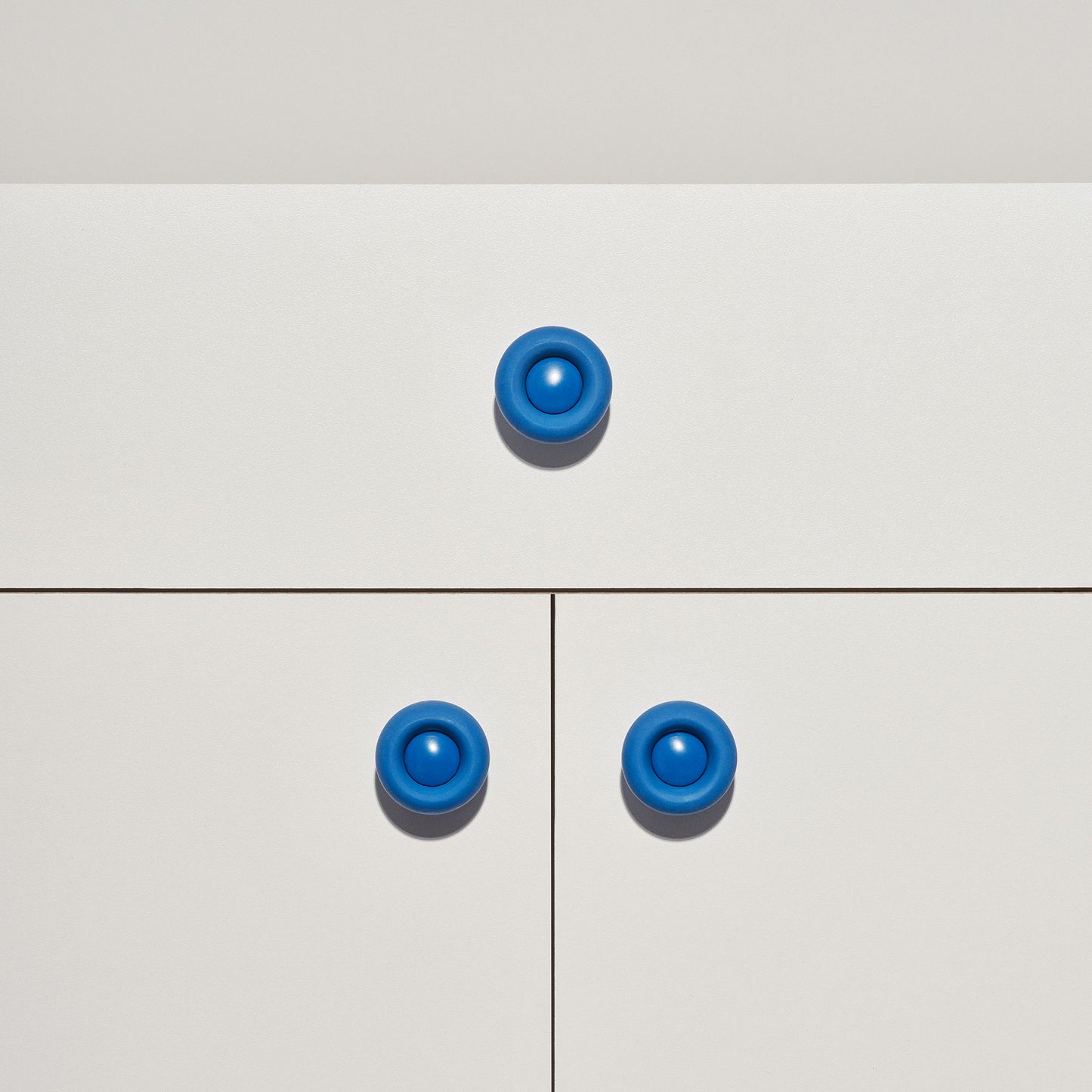 White cabinet with bright blue colored cabinet knobs on a white background