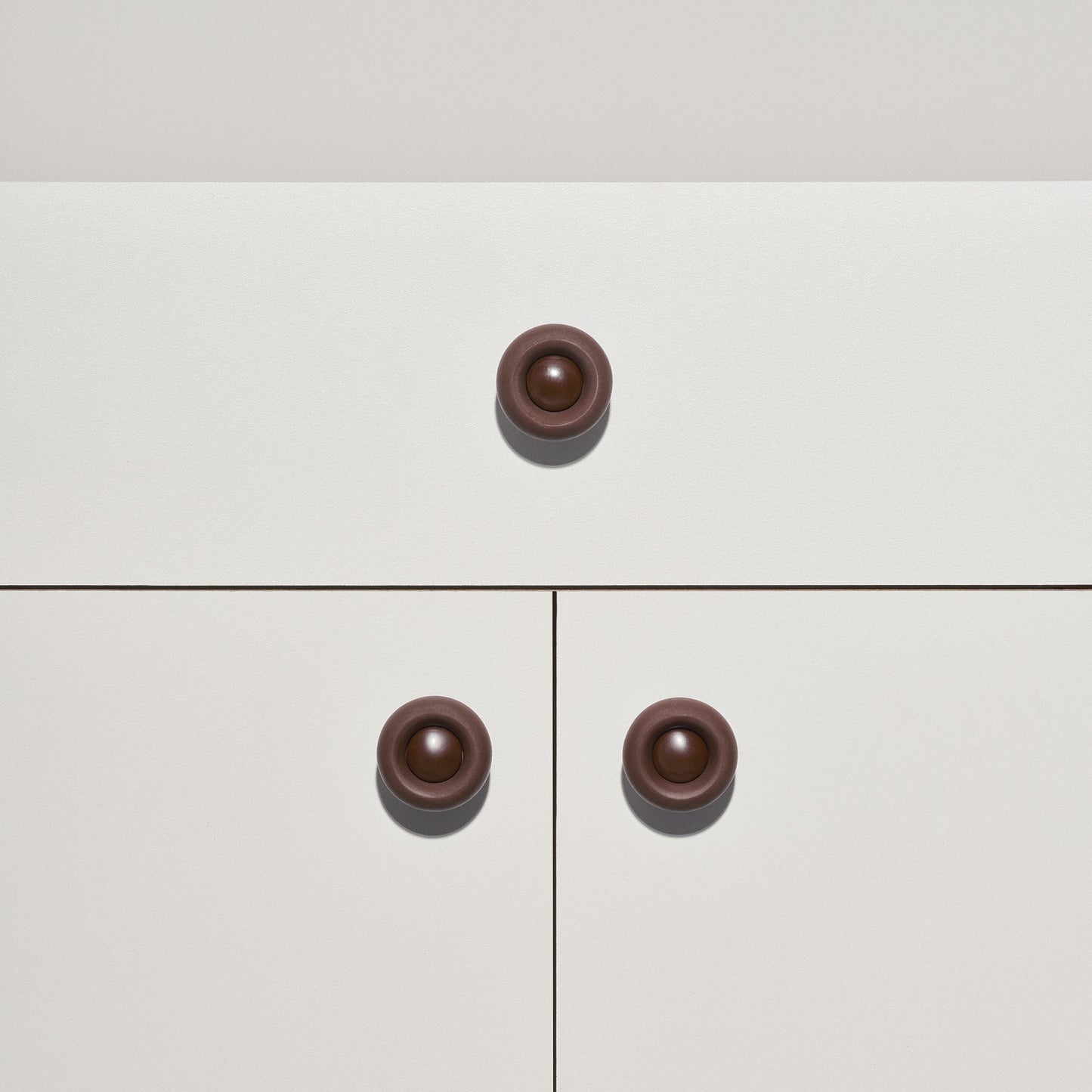White cabinet with chocolate brown  colored cabinet knobs on a white background